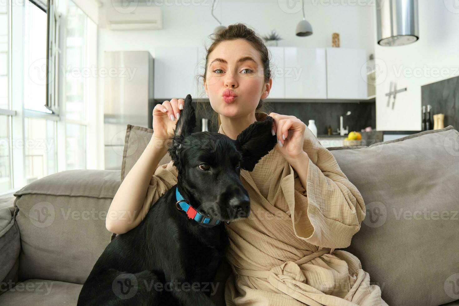 Portrait of happy girl playing with dogs ears, playing with her puppy on sofa photo