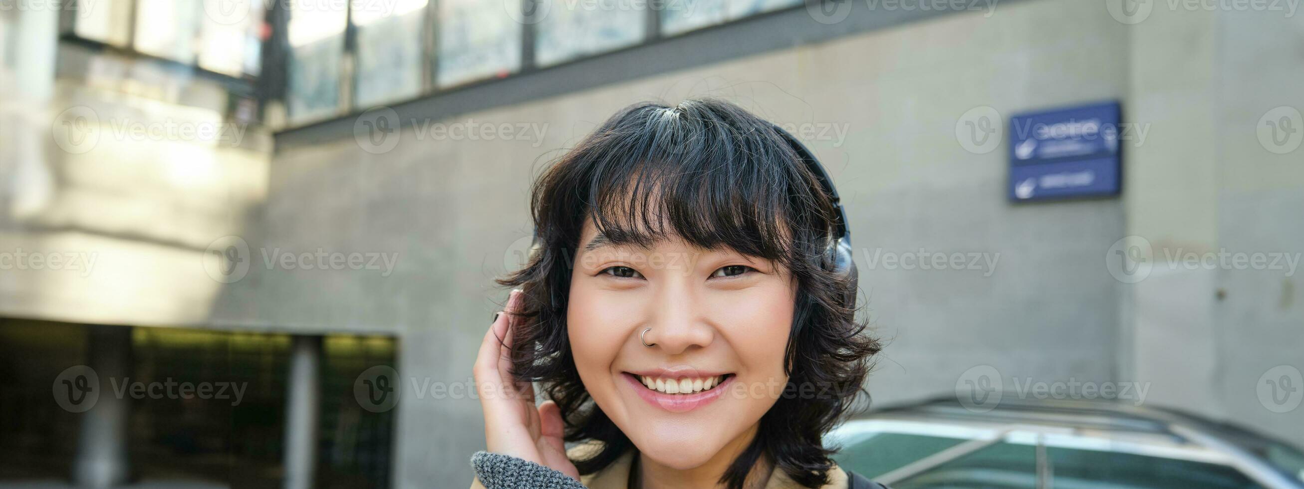 cerca arriba de sonriente morena niña en auriculares, escucha música, viajes alrededor ciudad, viaja a trabajar, soportes en un calle foto