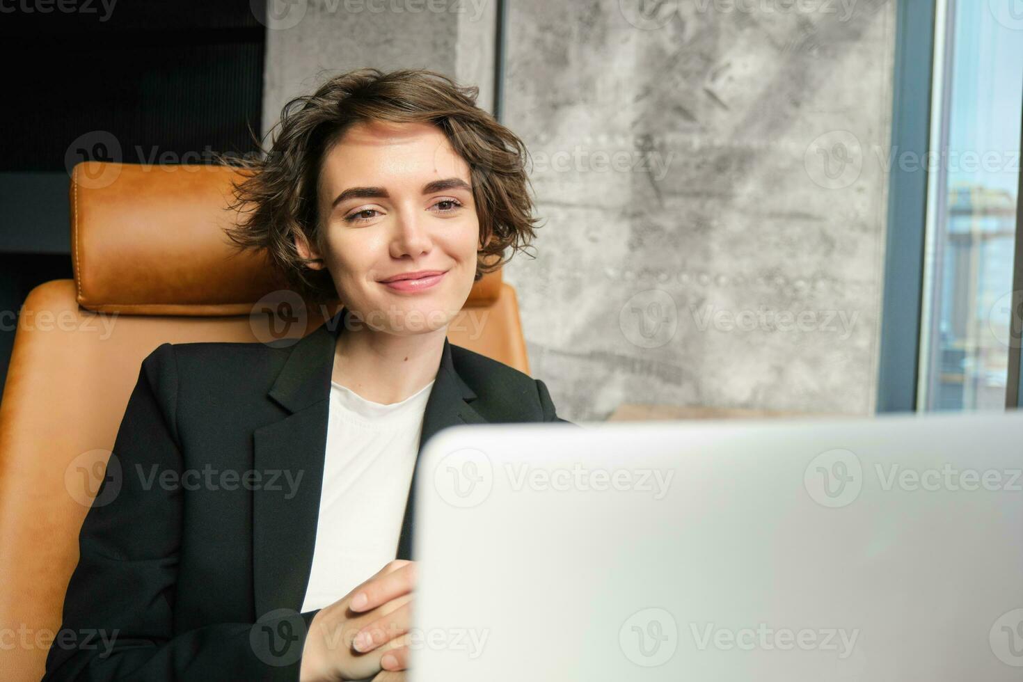 retrato de joven exitoso mujer de negocios dando presentación en línea, asistiendo seminario web en computadora portátil, sentado en oficina, mirando a computadora pantalla foto