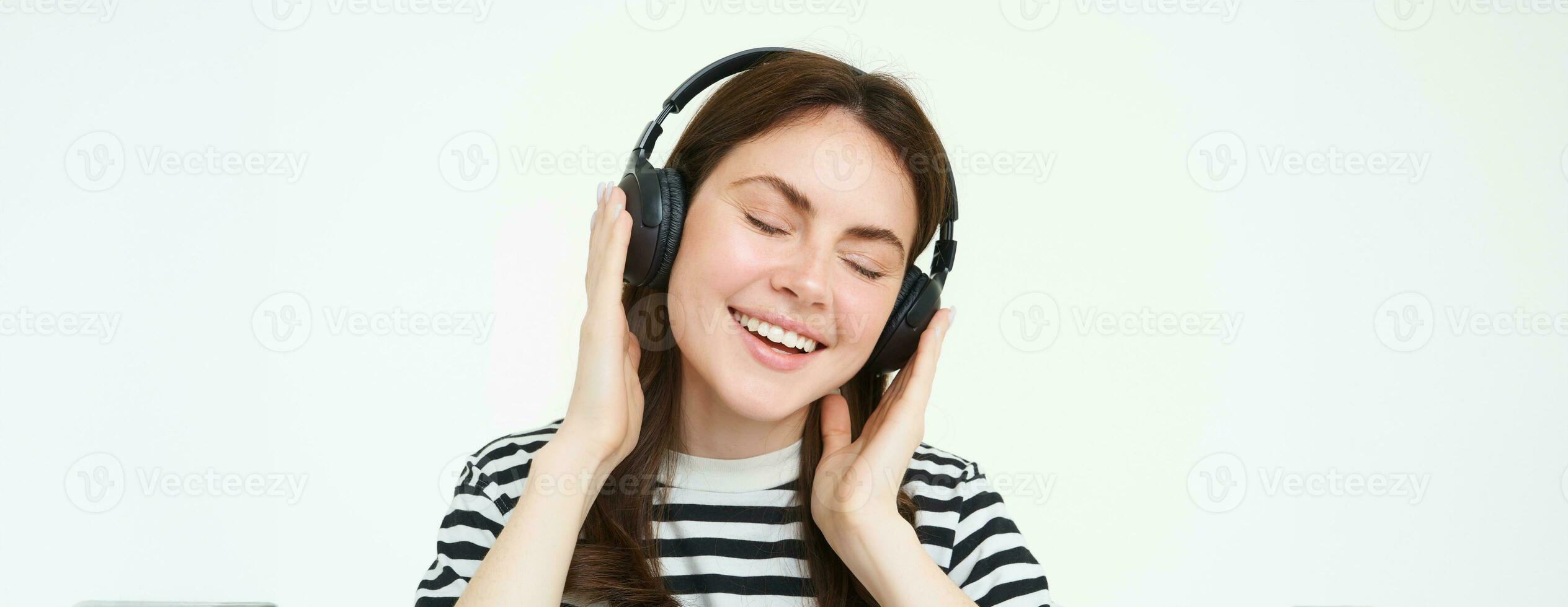 Portrait of beautiful woman in wireless headphones, listening music, using earphones, smiling at camera, standing over white background photo