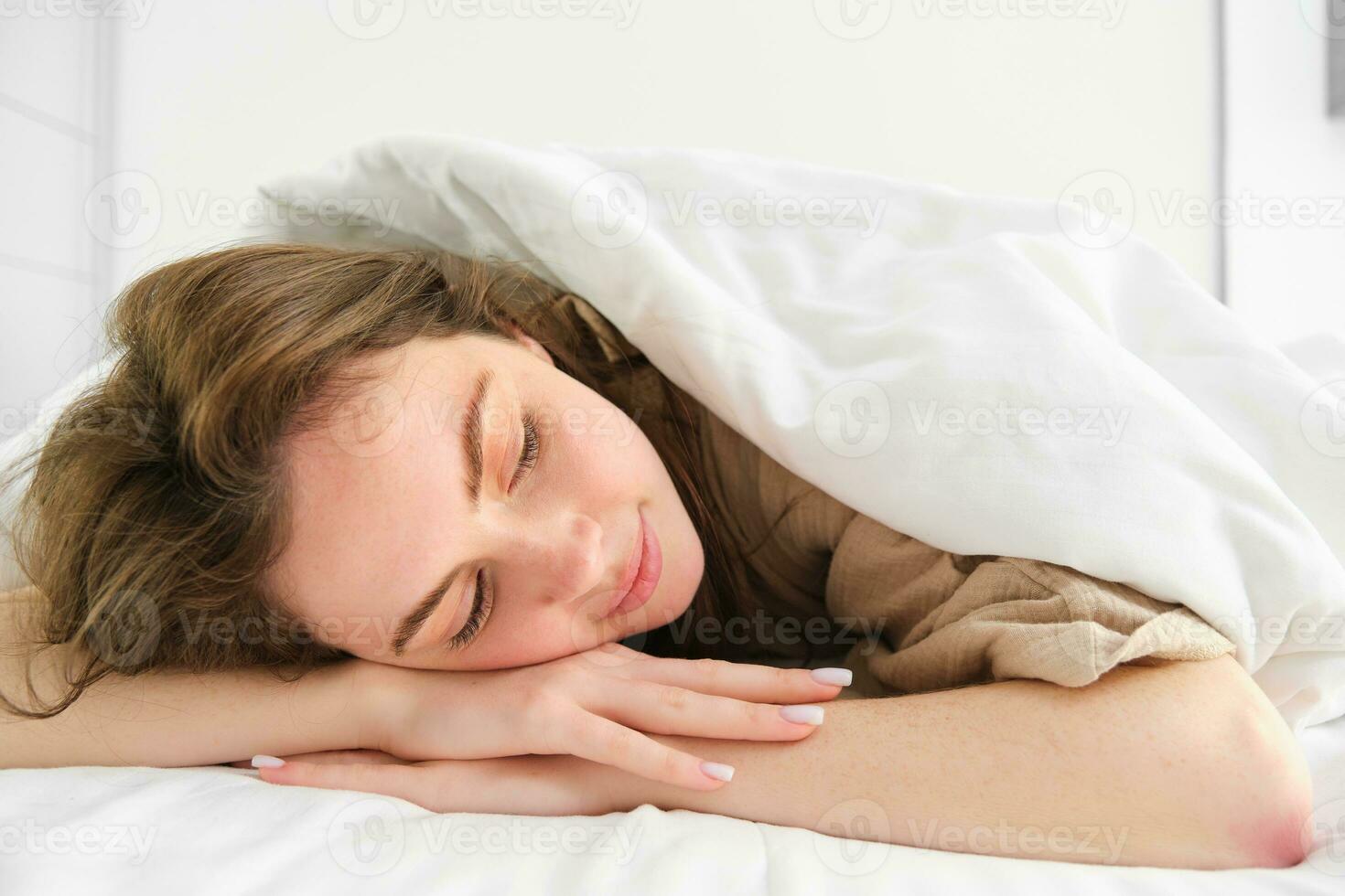 retrato de contento joven mujer dormido en su cama, disfrutando un siesta en hotel suite, acostado debajo cobija foto
