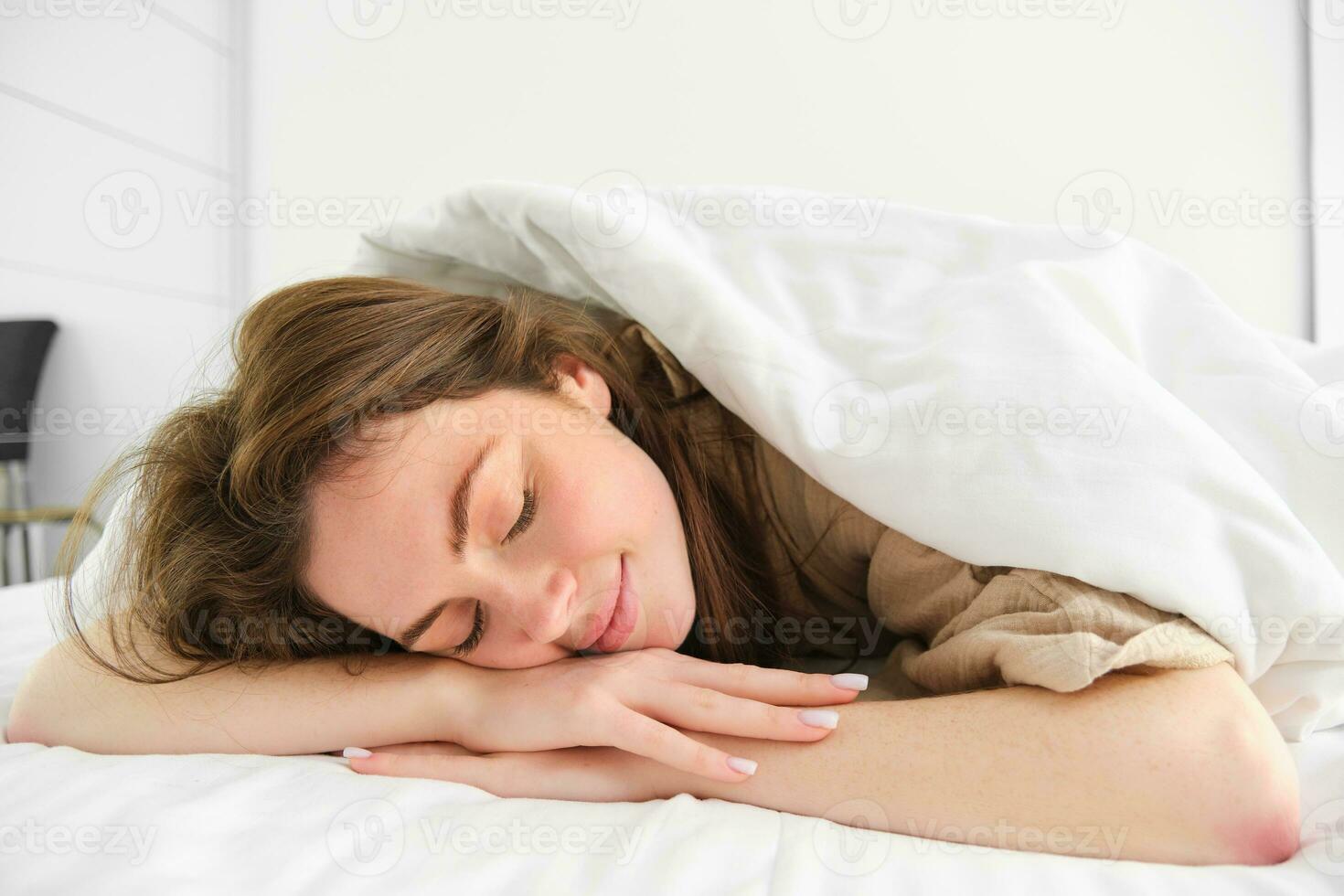 Cute young woman lying under blanket and smiling, sleeping, having a good morning nap, lazy day in bed photo