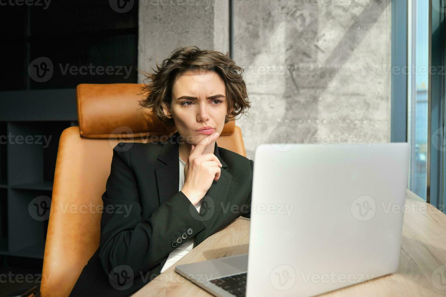 Portrait of working woman, businesswoman looking focused at laptop, thinking, frowning while solving issue at work photo