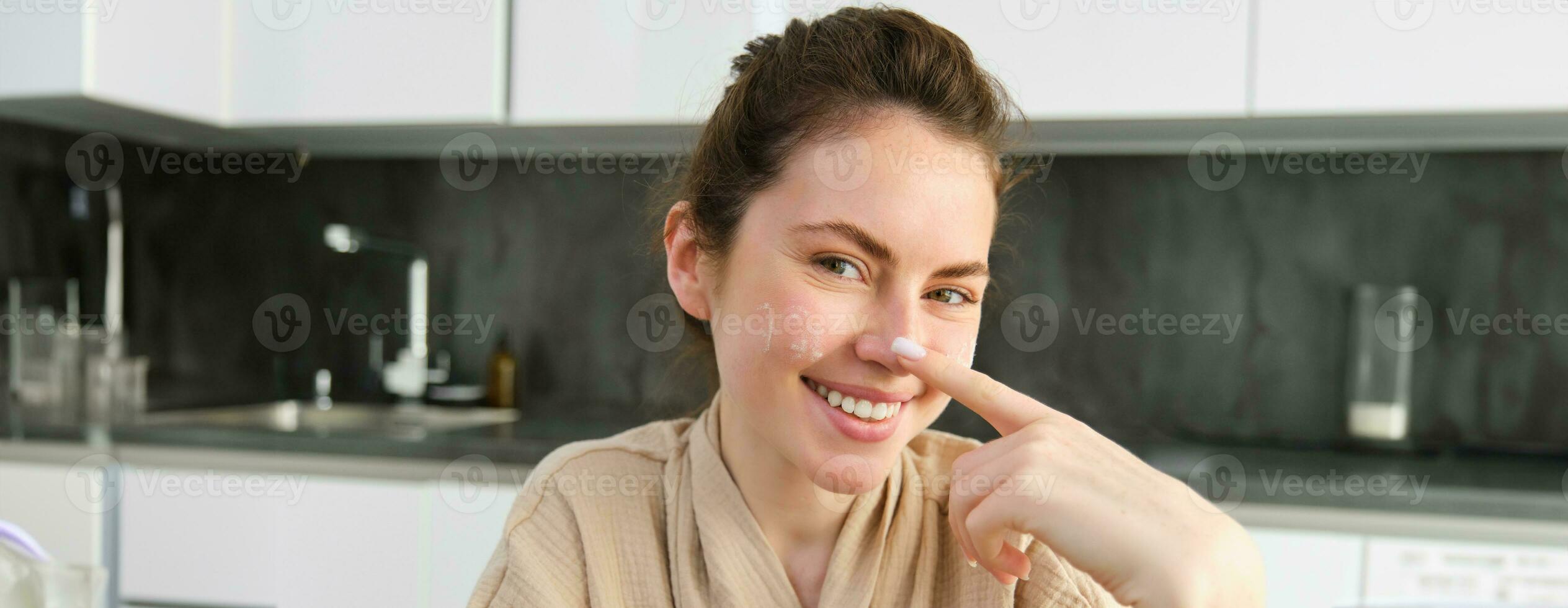 Attractive young cheerful girl baking at the kitchen, making dough, holding recipe book, having ideas photo