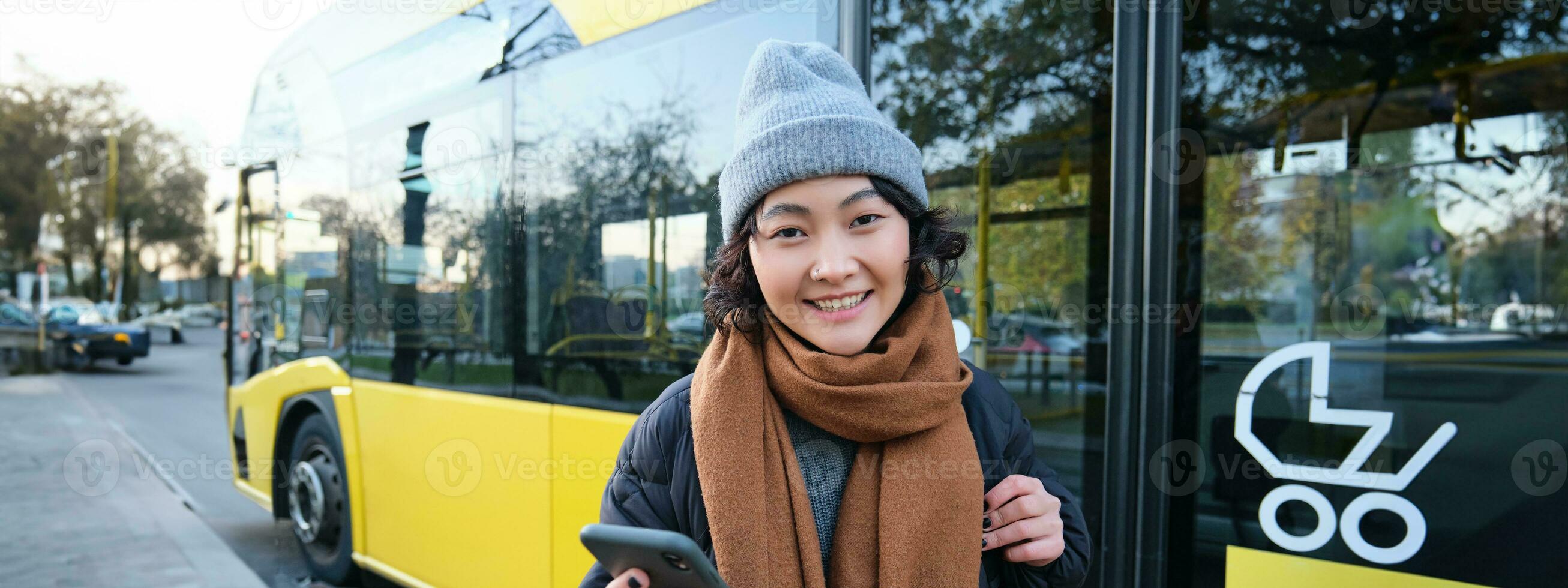 Image of girl student waiting for public transport, checks schedule on smartphone app, stands near city bus photo