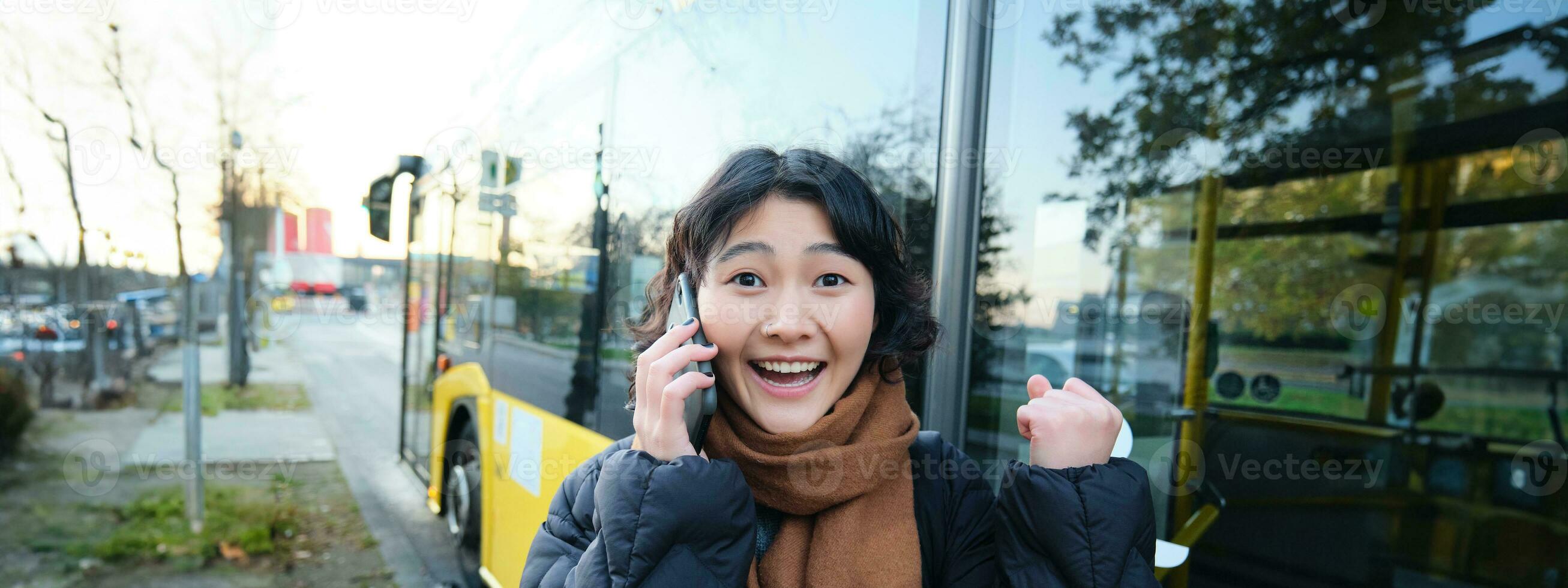contento asiático niña negociaciones en móvil teléfono y mira sorprendido, asombrado por genial noticias, lograr meta, oír alguna cosa emocionante foto
