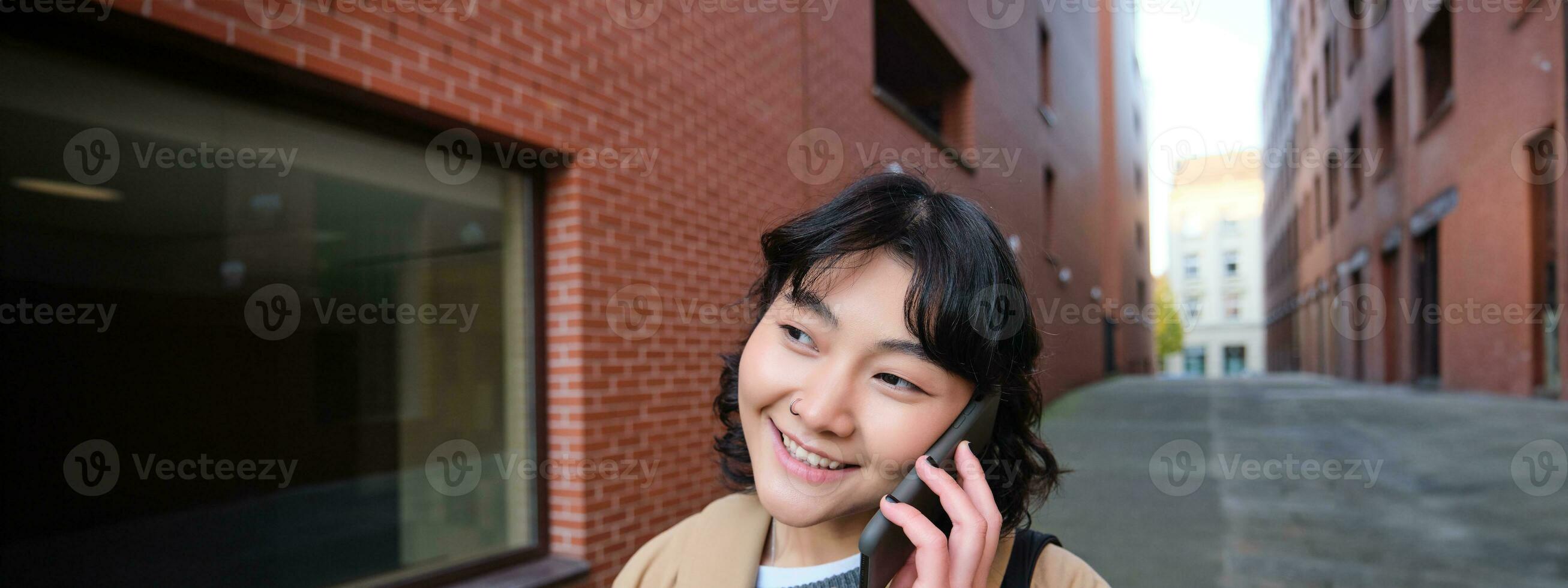 Cellular technology concept. Young modern girl talks on mobile phone, walks on street and smiles, has conversation over telephone photo