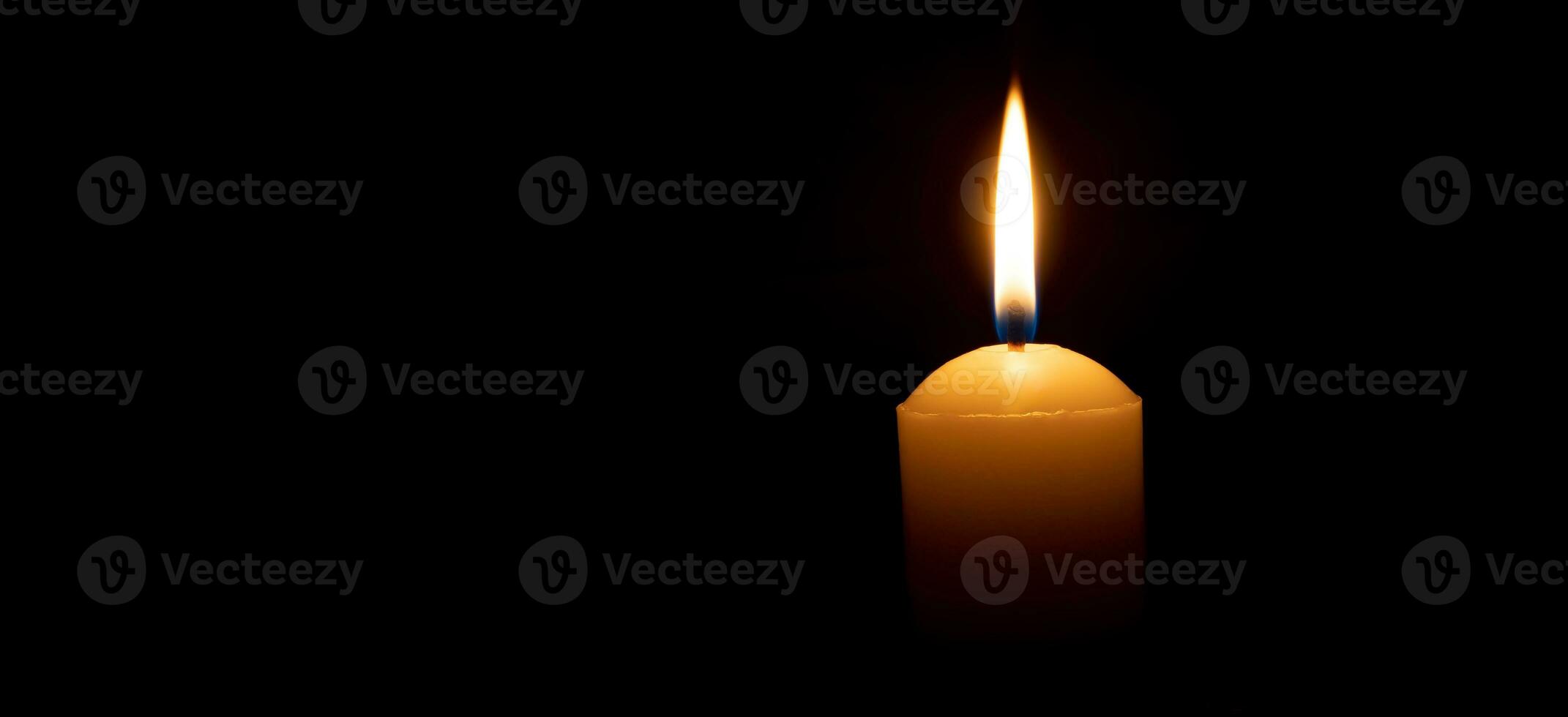 Single burning candle flame or light glowing on a big white candle on black or dark background on table in church for Christmas, funeral or memorial service with copy space photo