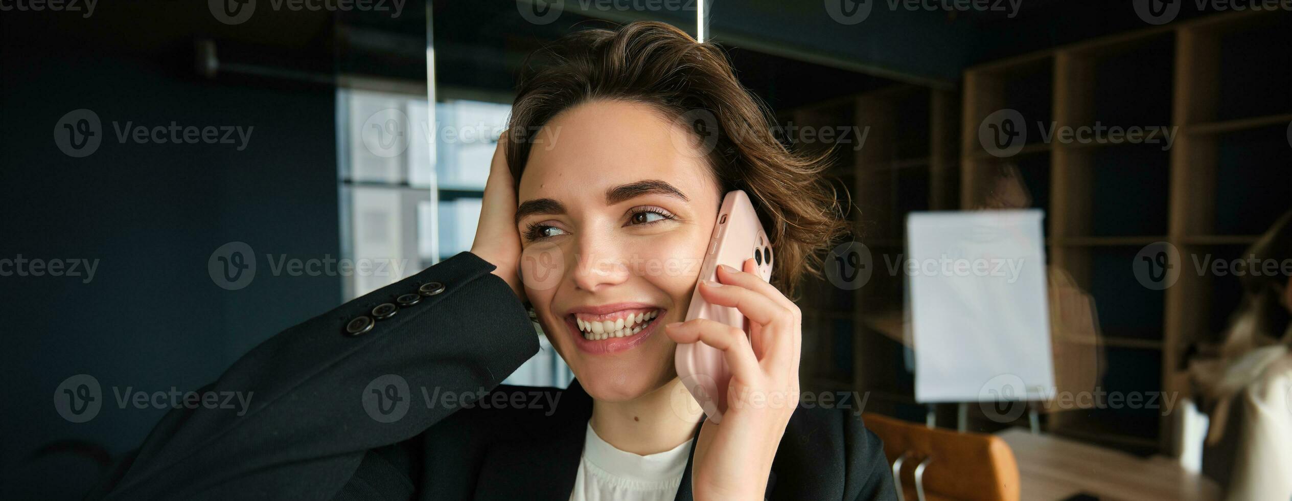 Close up portrait of happy woman in her office. Businesswoman answering a phone call with cheerful smile, receives great news over the telephone photo