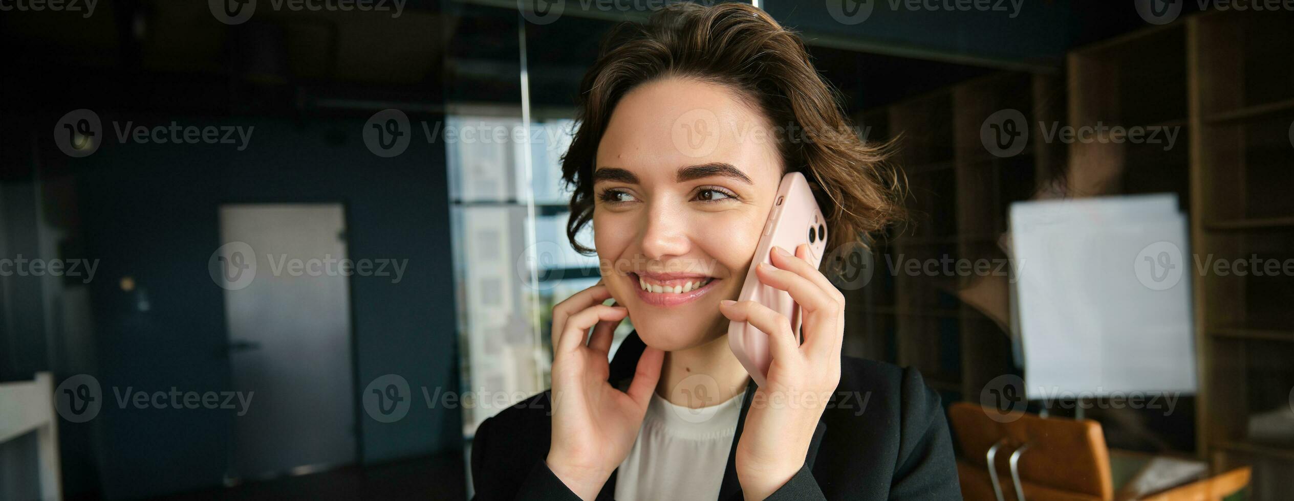 Close up portrait of happy woman in her office. Businesswoman answering a phone call with cheerful smile, receives great news over the telephone photo