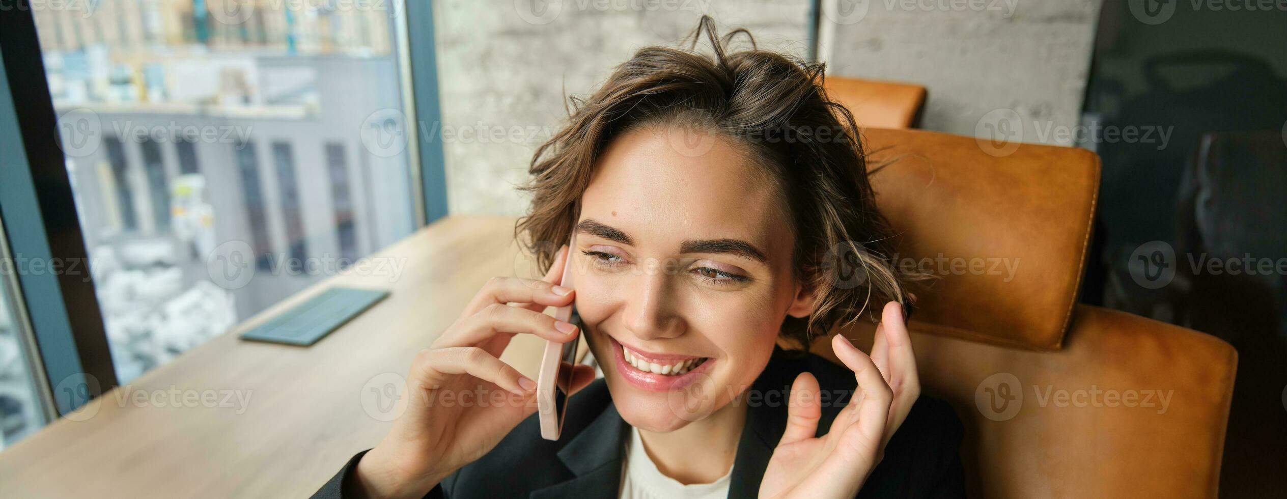 Image of successful woman talking on mobile phone, having a conversation over the telephone, answering client, sitting and working in an office photo