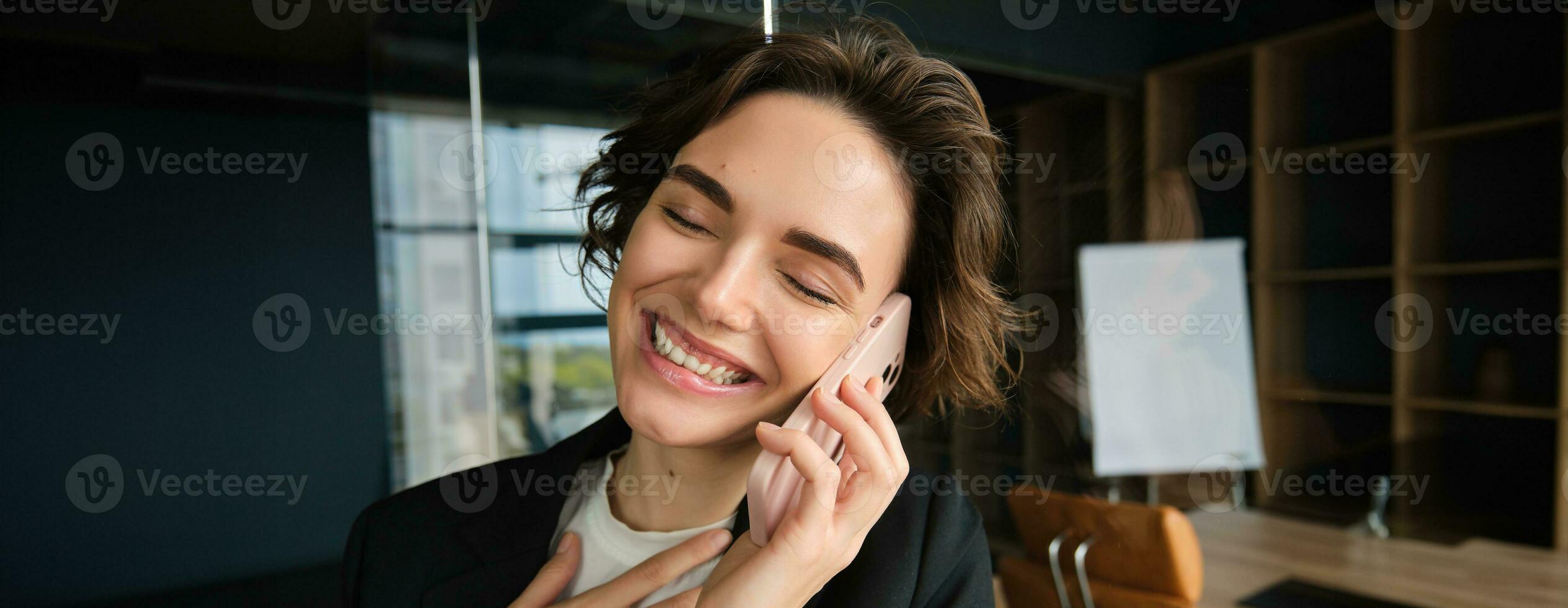 Close up portrait of happy woman in her office. Businesswoman answering a phone call with cheerful smile, receives great news over the telephone photo