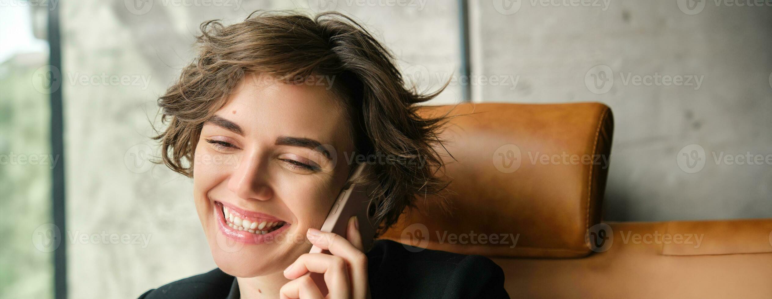 Corporate people and business concept. Young woman in suit, sitting in office and having conversation, answering phone call and smiling, talking to client photo