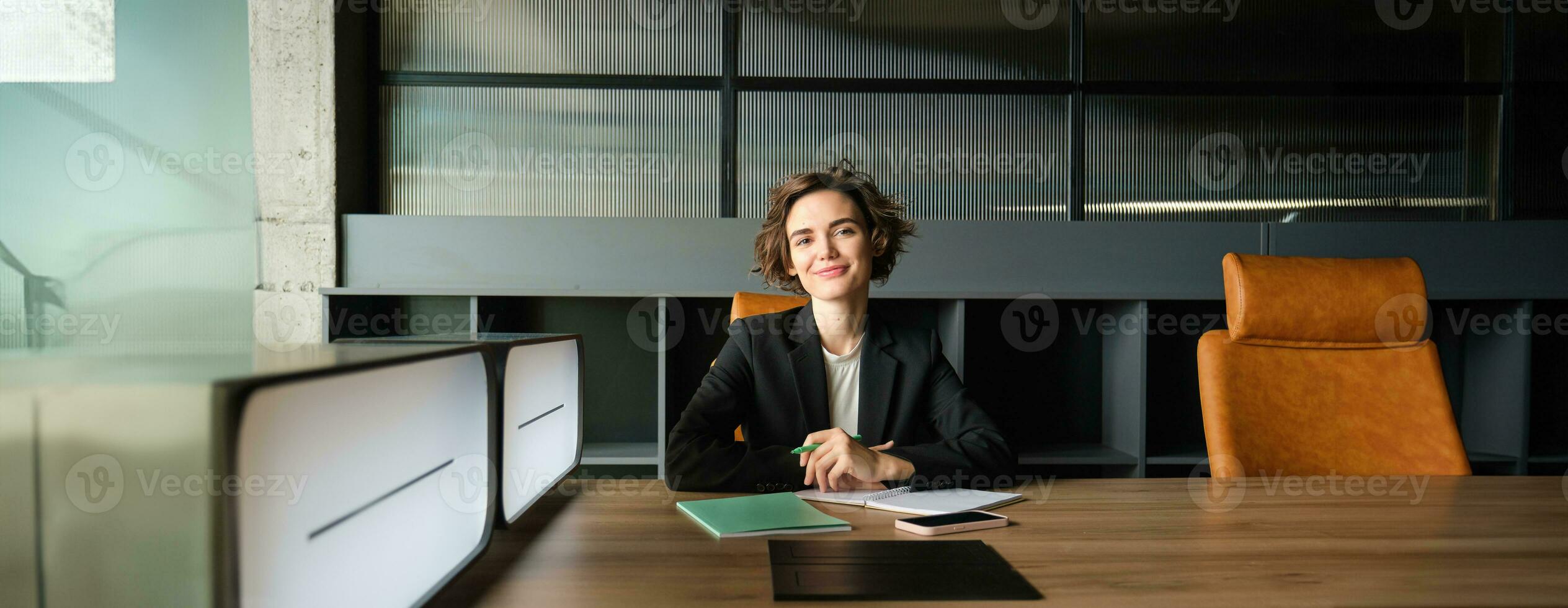 Portrait of businesswoman in suit, working on documents in an office, smiling at camera, looking confident photo