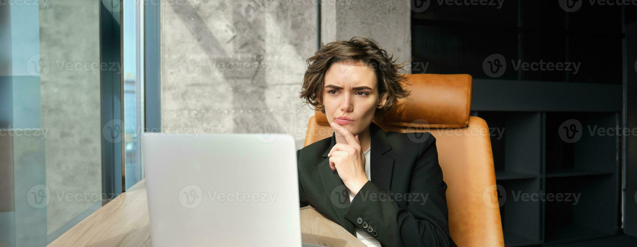 Portrait of working woman, businesswoman looking focused at laptop, thinking, frowning while solving issue at work photo