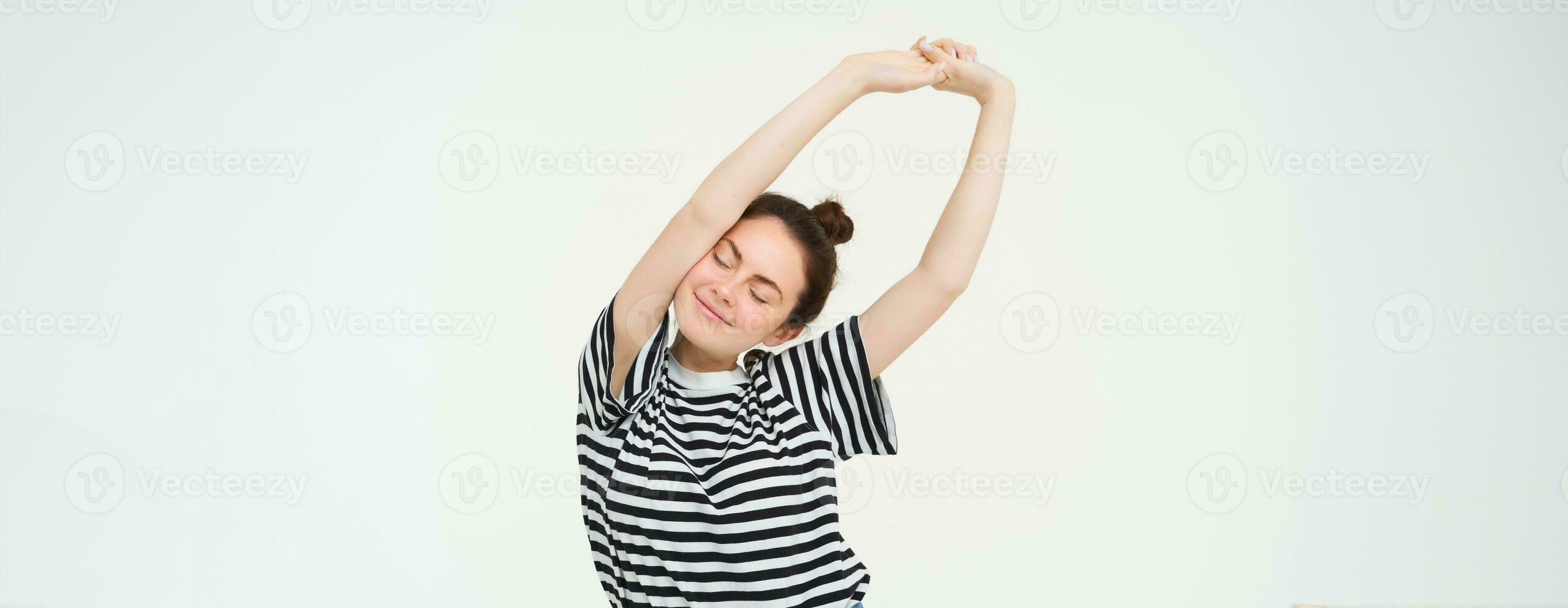 Portrait of happy young woman, stretching arms with pleased smile after good nap, standing over white background photo