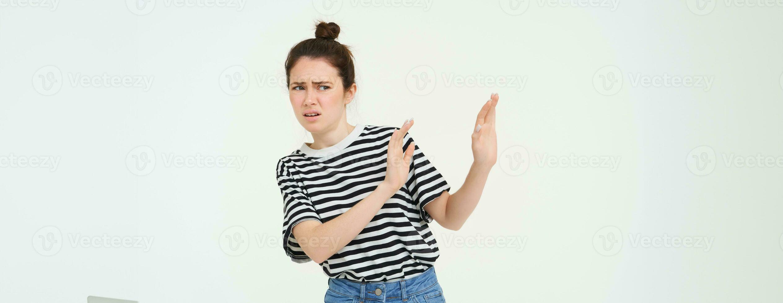 Image of woman expressing aversion, dislike something, looks apalled, extends hands forward in defensive gesture, rejecting, refusing, standing over white background photo