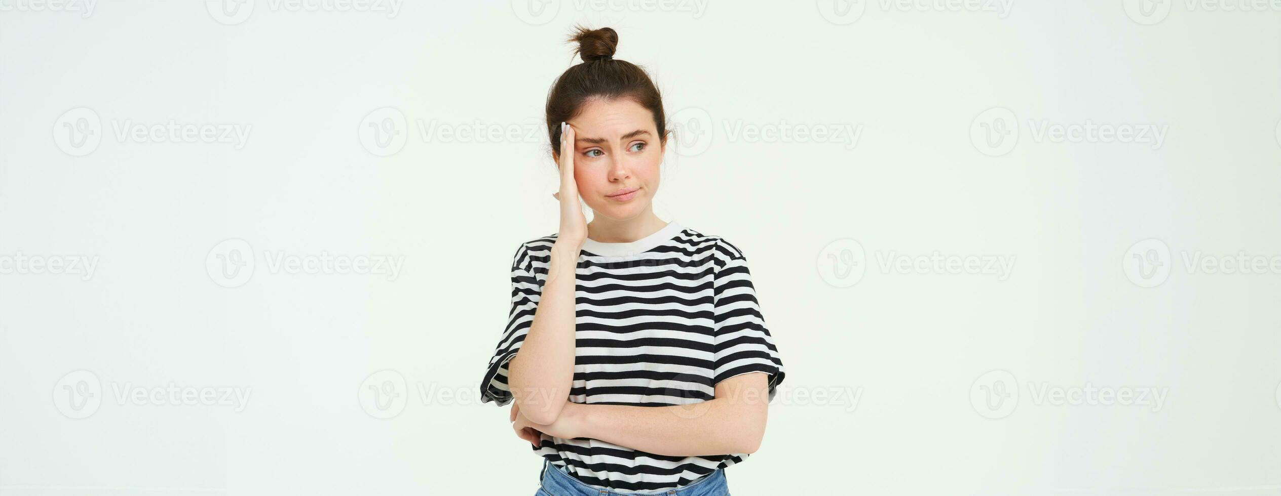 Portrait of concerned, worried young woman, touches her head, looking complicated, standing over white background photo