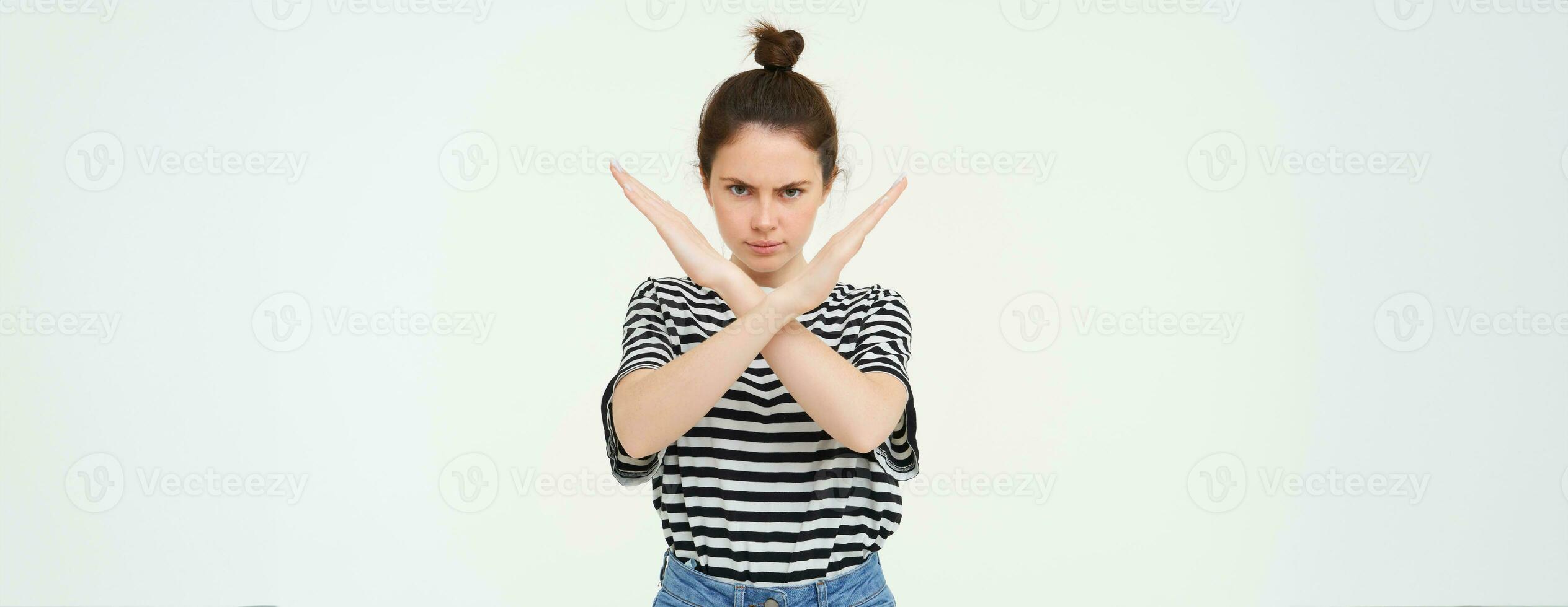 Portrait of young serious woman, shows cross, stop gesture, prohibit something, expresses her disapproval, stands over white background photo