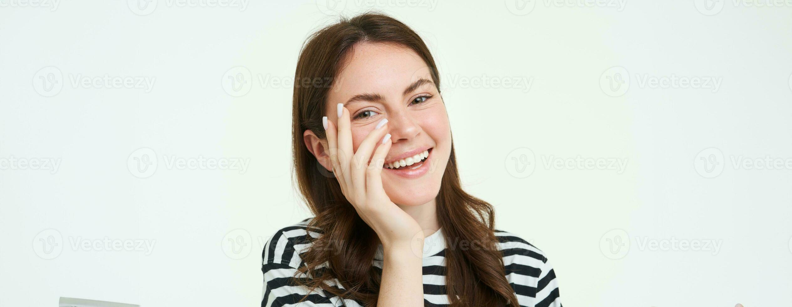 Lifestyle. Happy young woman laughing, touching her face and smiling at camera, white background photo