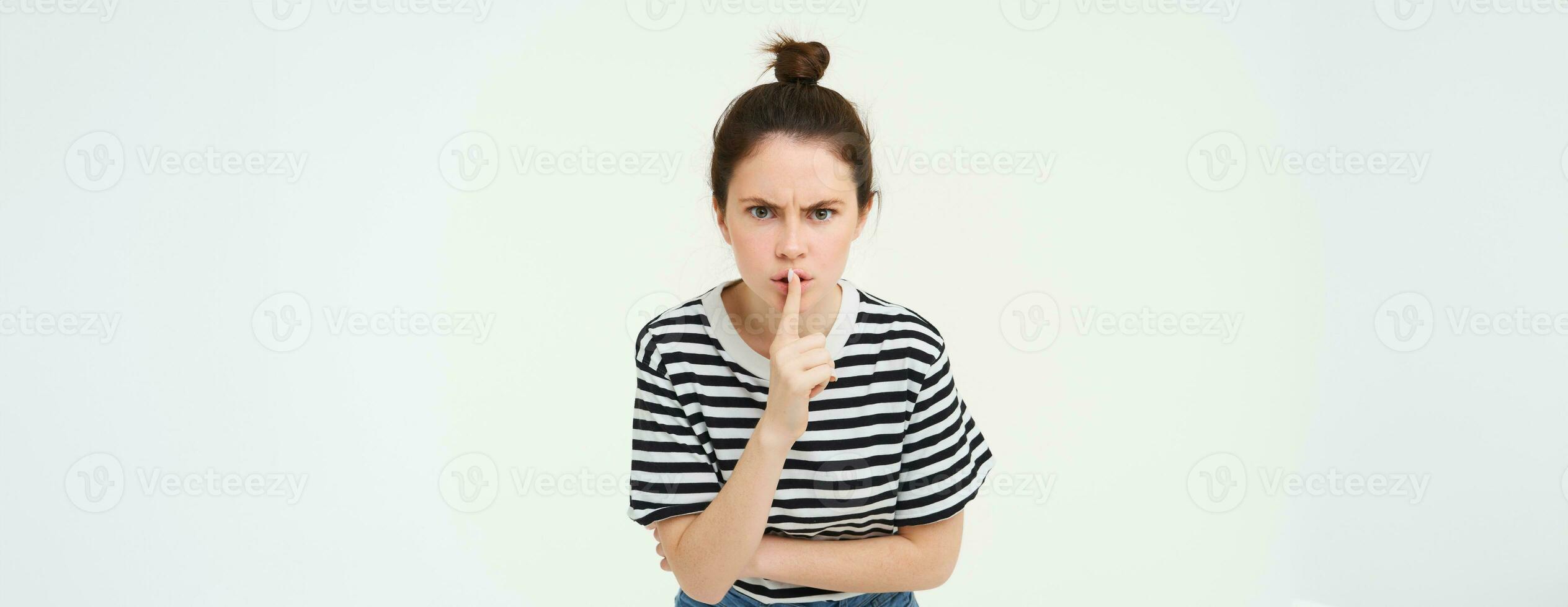 Image of angry woman shushing, makes hush gesture, press finger to lips with frustrated face, keep quiet, scolding loud person, white background photo