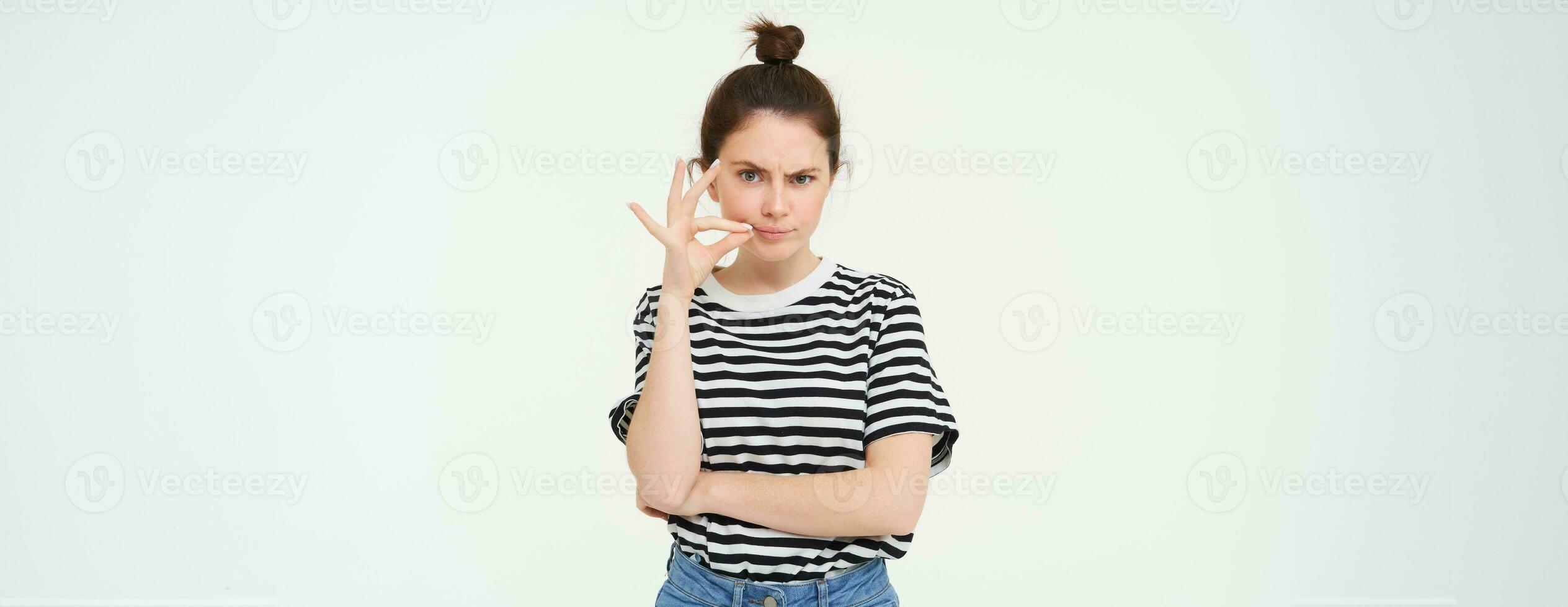 Young woman with doubtful face, zips her lips, seals mouth, promise not to tell anyone, isolated over white background photo