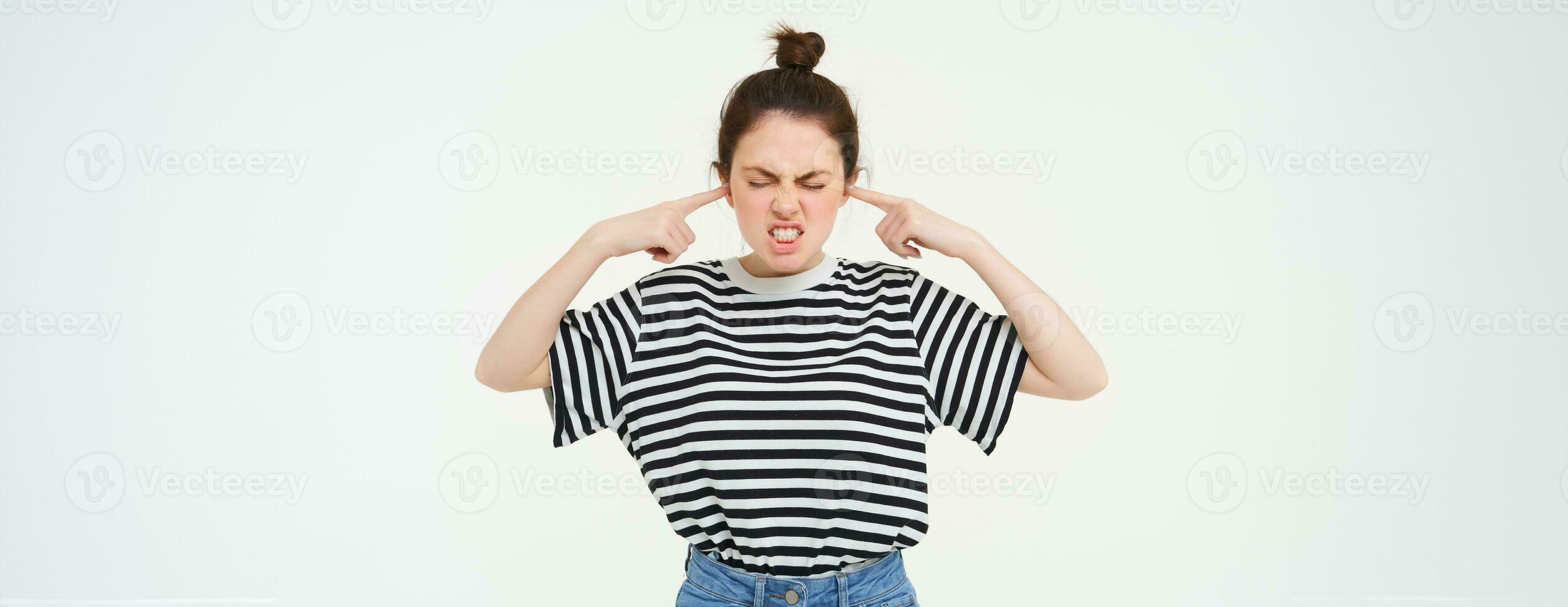 Image of annoyed woman shuts her ears, cant stand noise, being disturbed by loud music, stands over white background photo