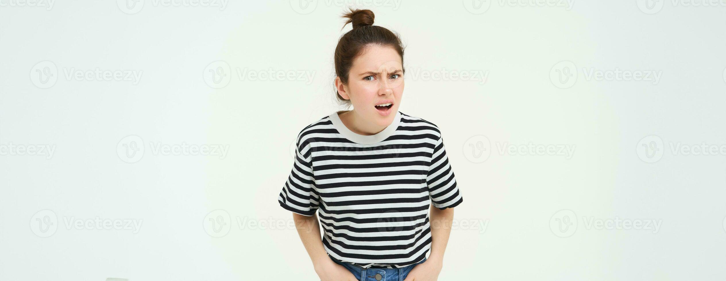 Portrait of young woman with shocked, angry face expression, hear something disappointing, shows negative, frustrated reaction, standing over white background photo