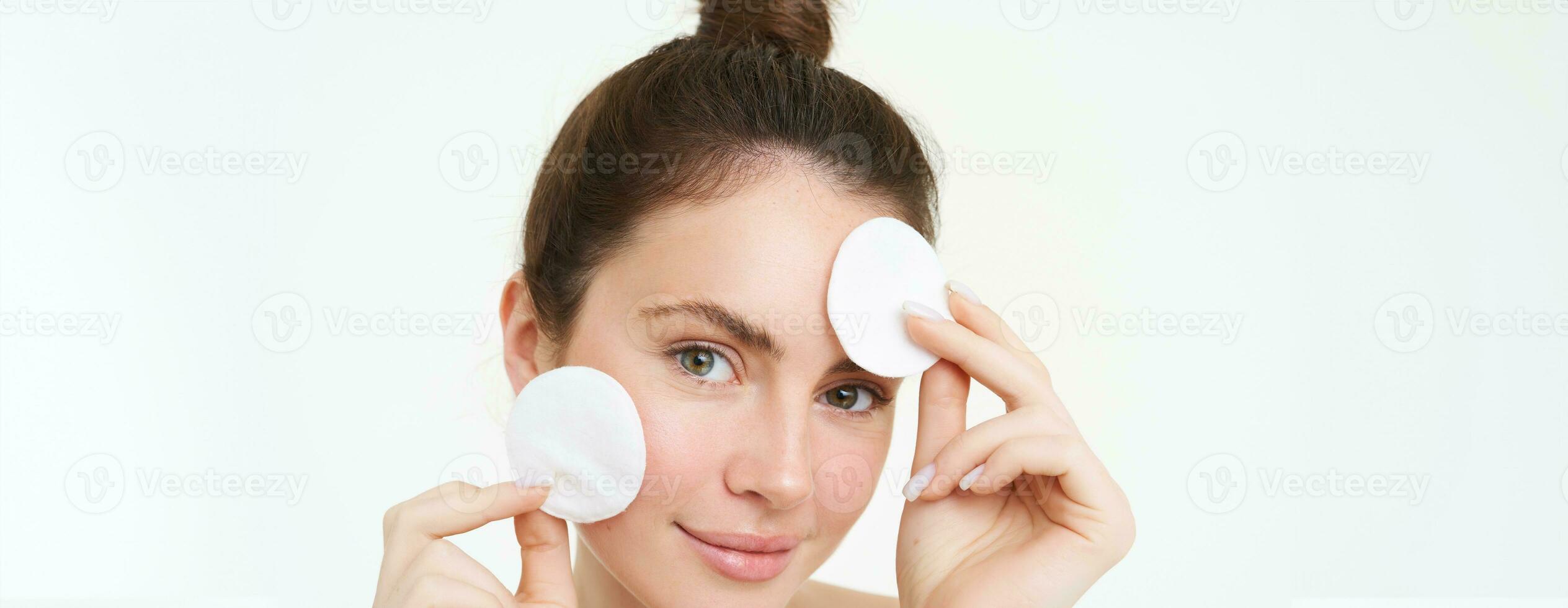 Portrait of young woman cleansing her face, takes off her makeup, washing her face, using skincare routine with cotton pads, isolated over white background photo