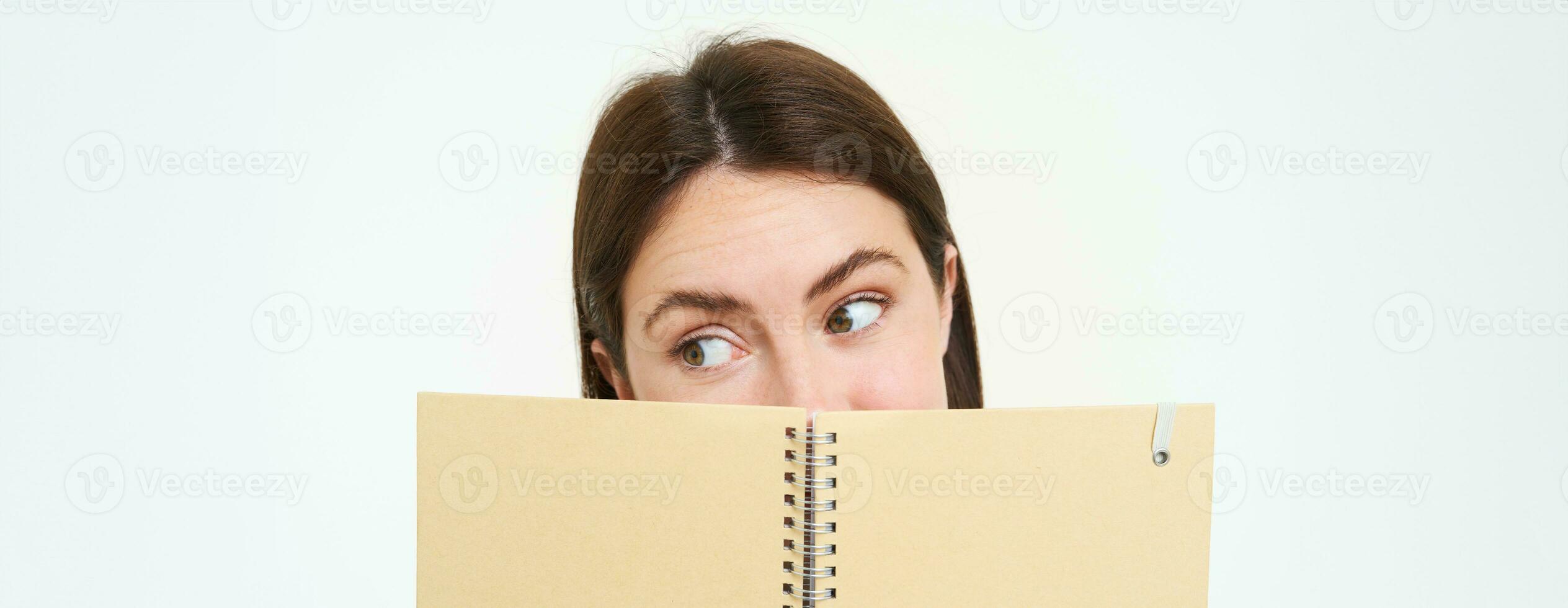 Image of woman reading something interesting in notebook, holding planner and making a side eye, standing over white background photo