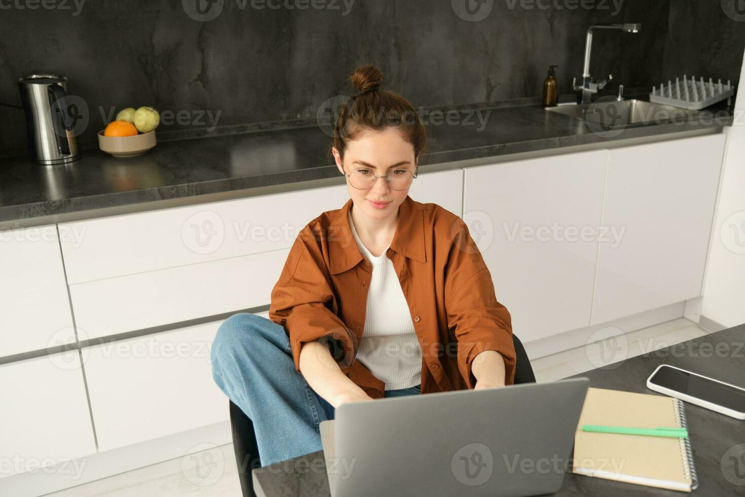 Portrait of beautiful young woman studying at home, sitting with laptop and documents in kitchen. Self-employed business owner typing on computer, sending emails to clients photo