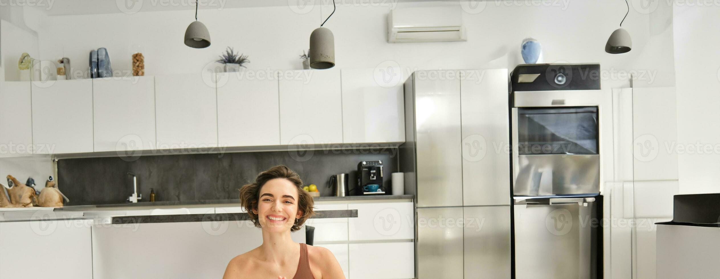 Vertical portrait of young woman, fitness instructor, mindfulness coach sitting on floor at home in lotus pose, meditating, doing yoga workout photo