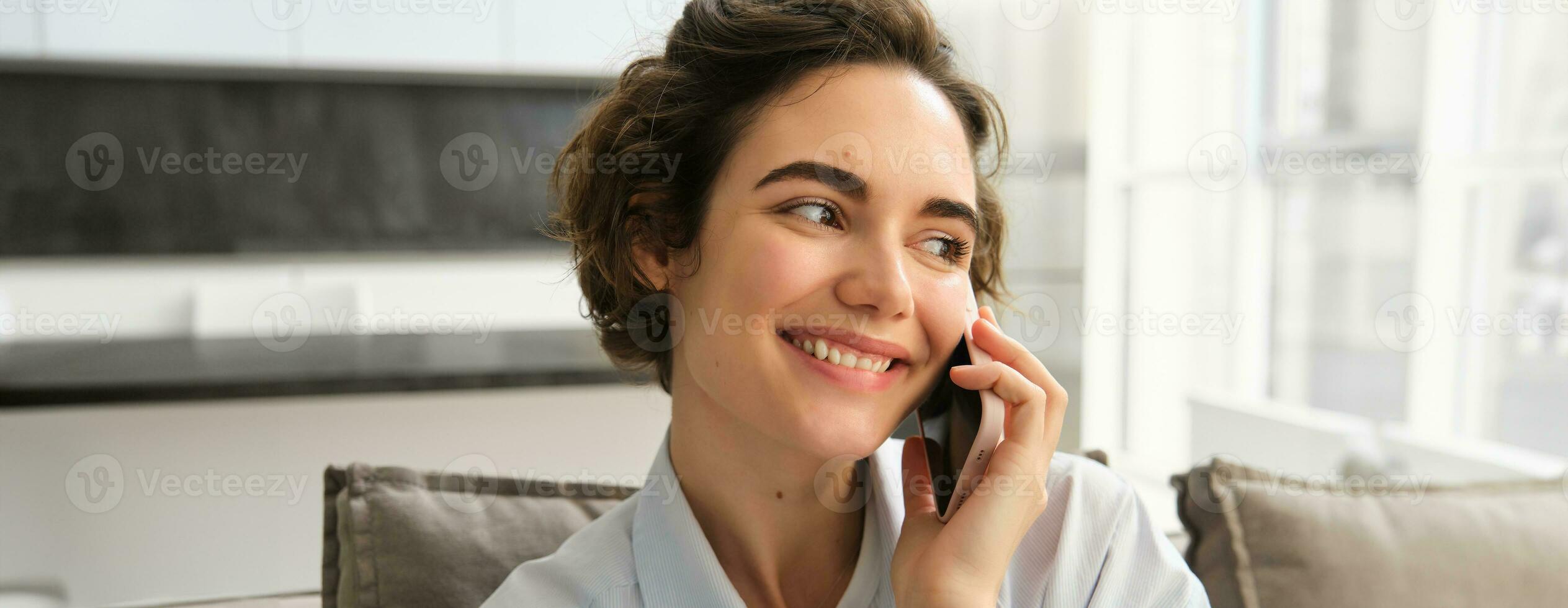 Close up portrait of smiling beautiful woman, talking on mobile phone, chats on smartphone, calls someone, sits at home photo