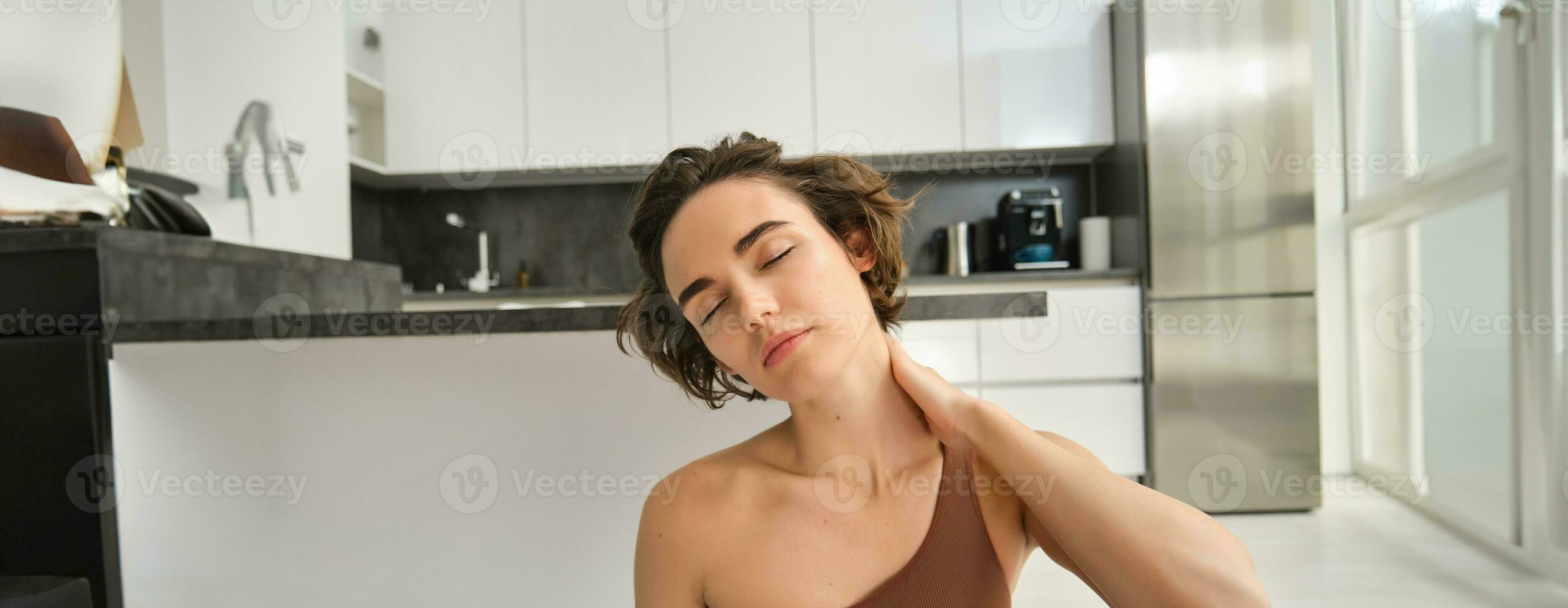 Close up portrait of sportswoman, fitness woman massaging her neck, warm-up her body after workout, doing yoga on rubber mat at home photo