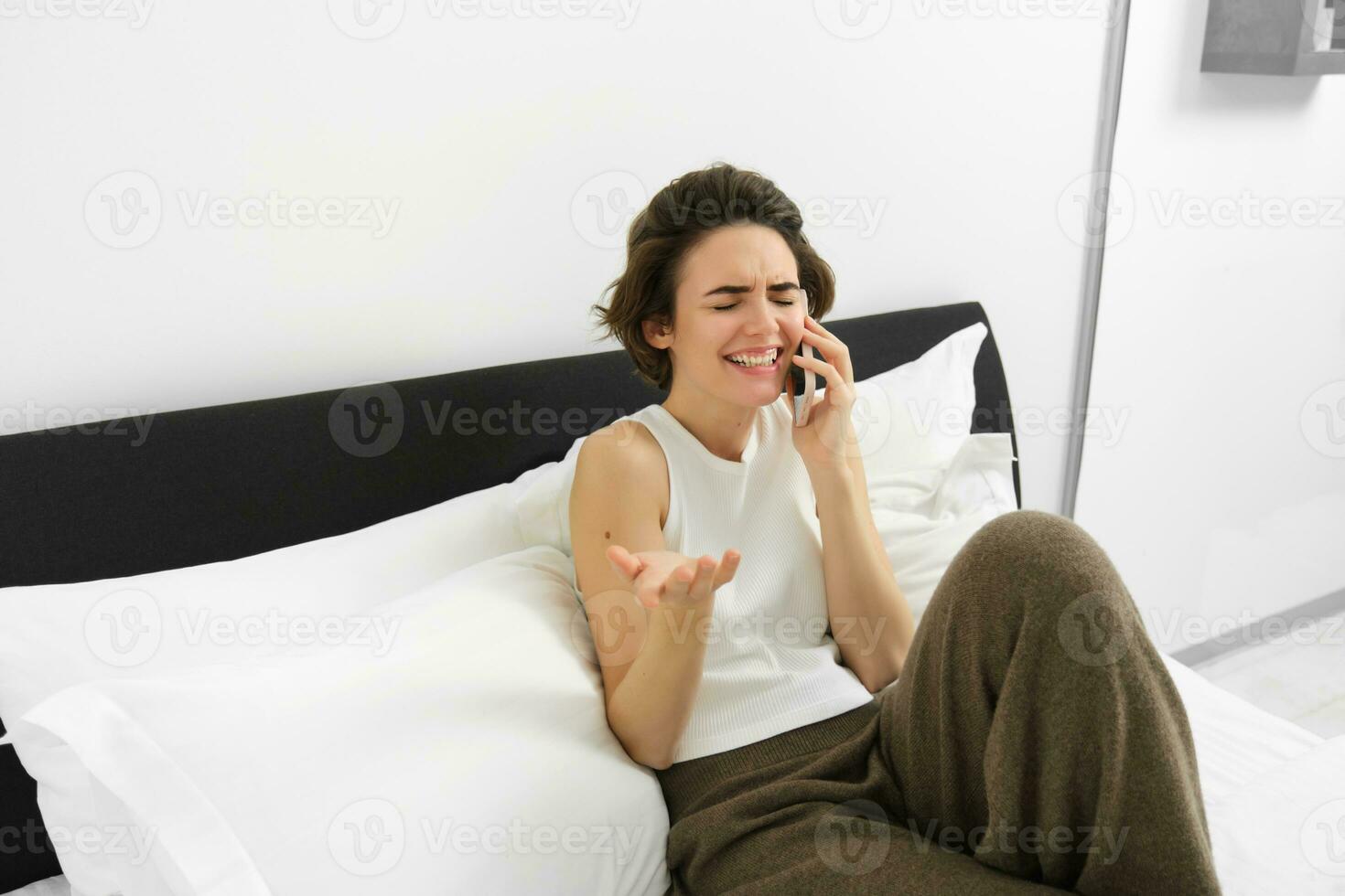 hablador joven mujer reír, hablando en teléfono, vocación amigo, acostado en cama y teniendo conversacion con alguien, descansando en dormitorio foto