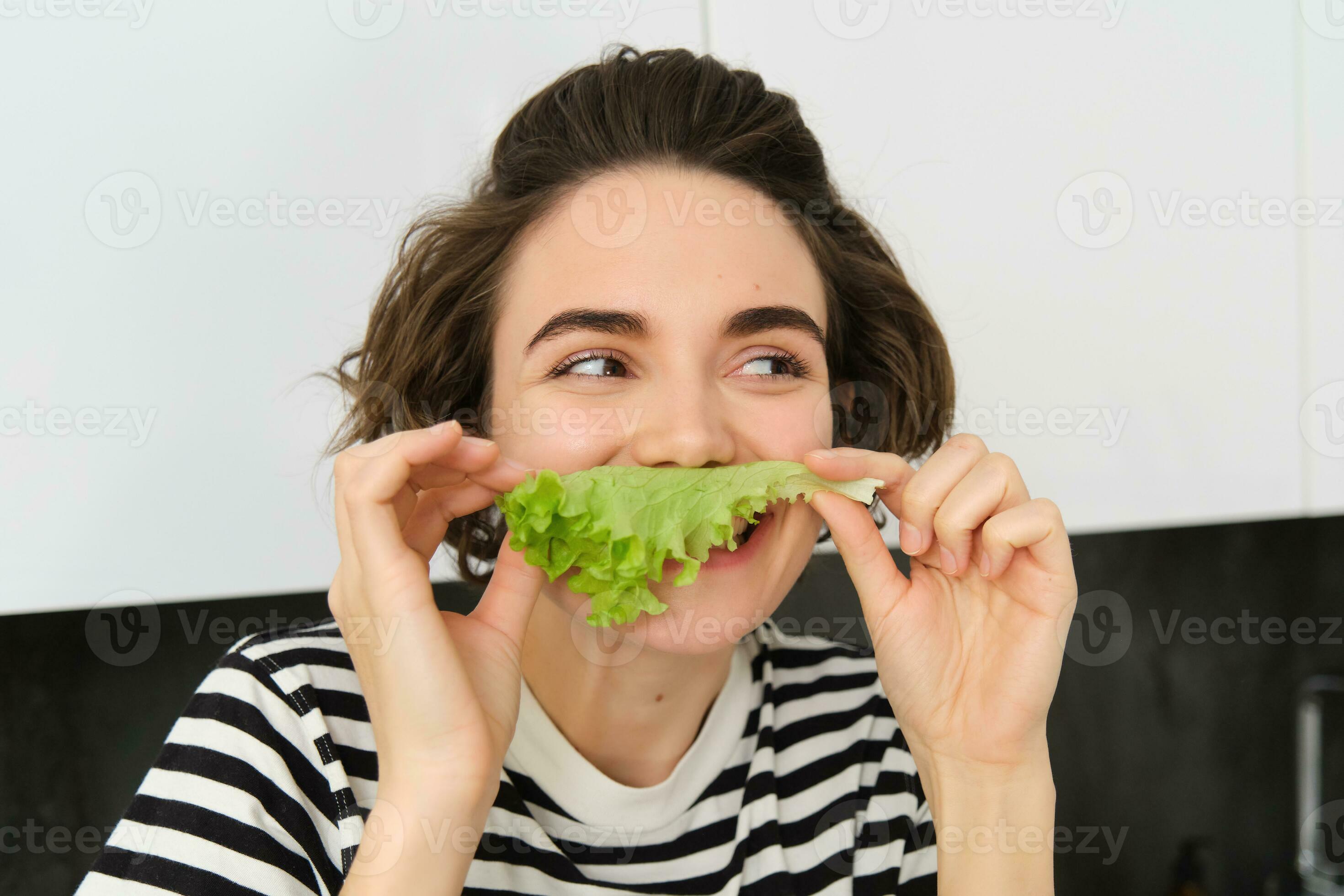Cute smiling woman eating lettuce leaf and smiling, having a healthy snack, likes vegetables
