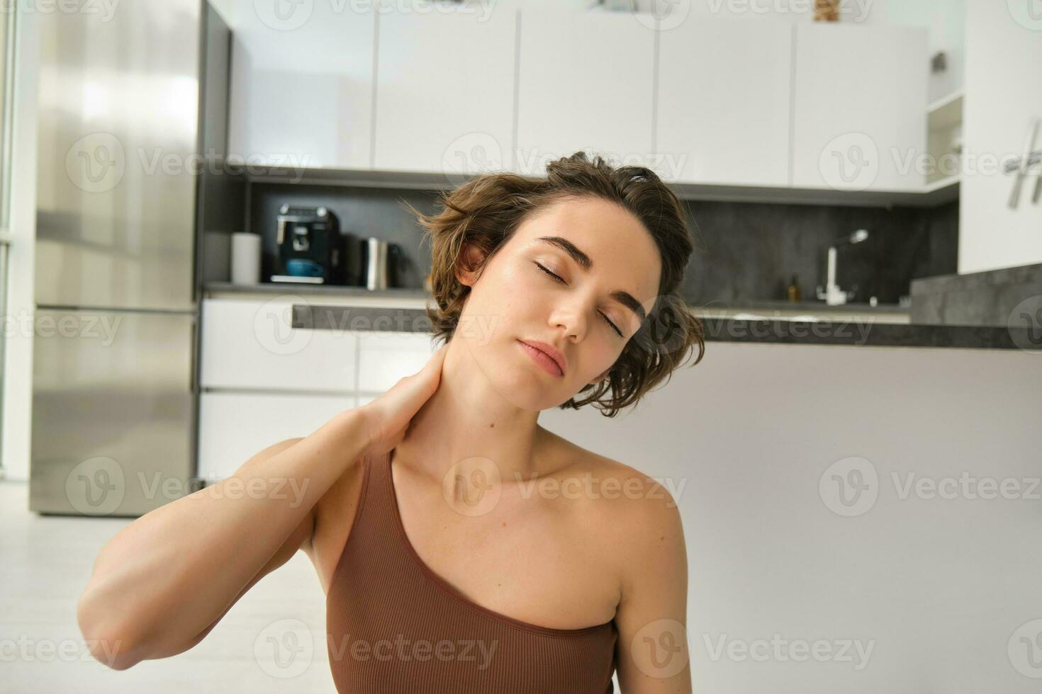 Close up portrait of sportswoman, fitness woman massaging her neck, warm-up her body after workout, doing yoga on rubber mat at home photo