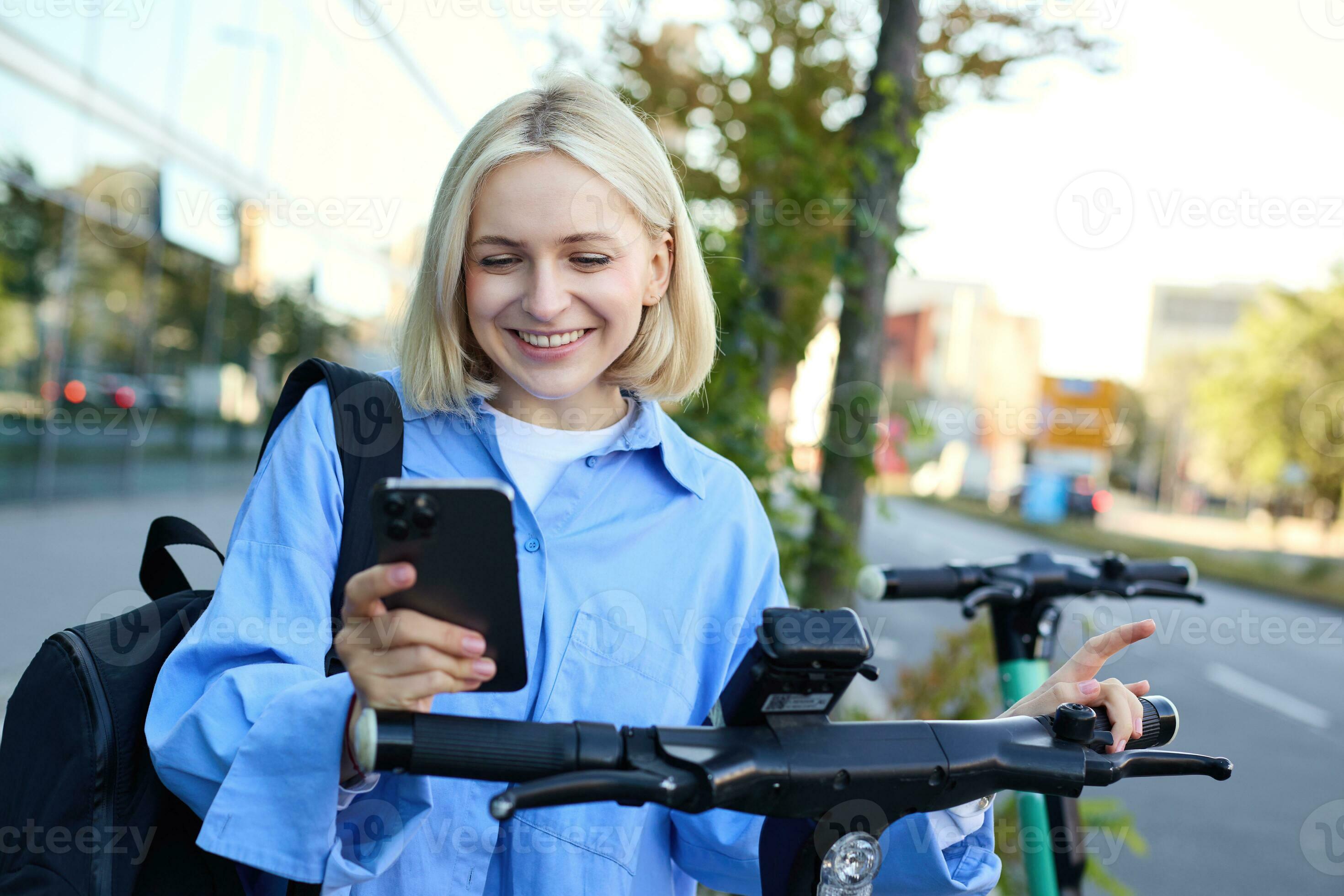 Mujer joven montando una bicicleta eléctrica y utilizando el teléfono móvil