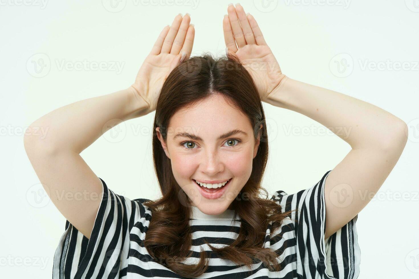 Image of cute brunette girl shows animal eats with hands on top of head, smiling and looking happy, white background photo