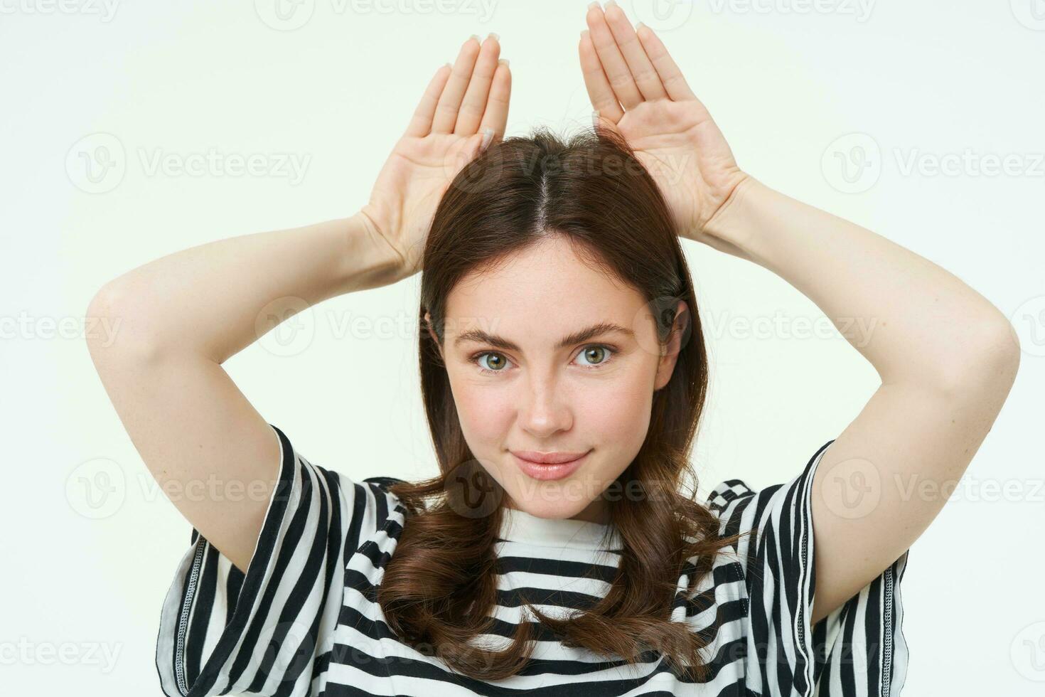 Image of cute brunette girl shows animal eats with hands on top of head, smiling and looking happy, white background photo