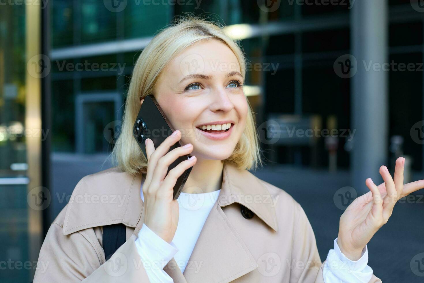 Close up portrait of young blond woman, walking on street and talking on mobile phone, chatting with friend on smartphone photo