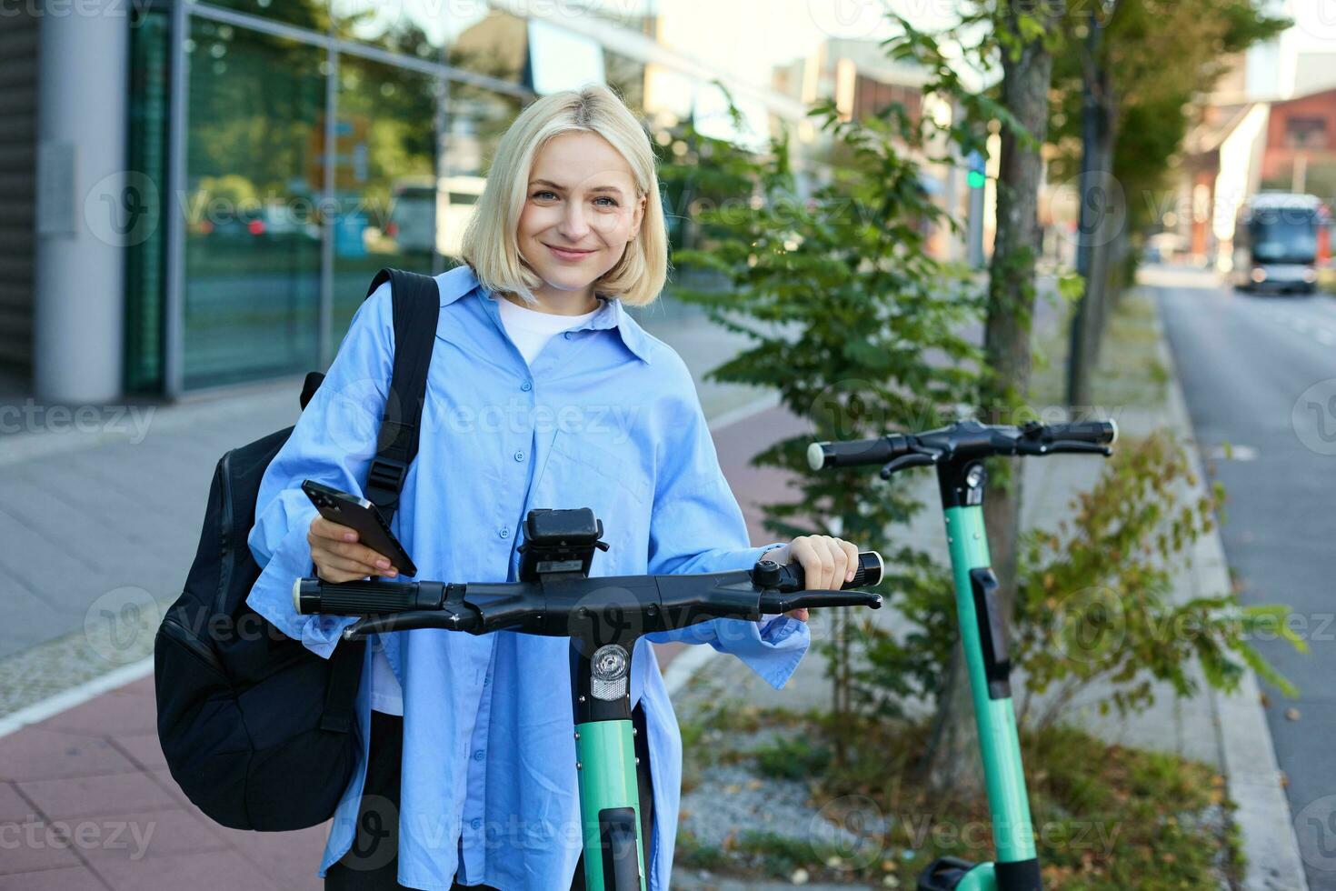 Woman Scanning QR Code on Handlebar of Shared Electric Scooter. Close up of Female Hand Holding Smartphone Unlocking Green E-Scooter in Street photo