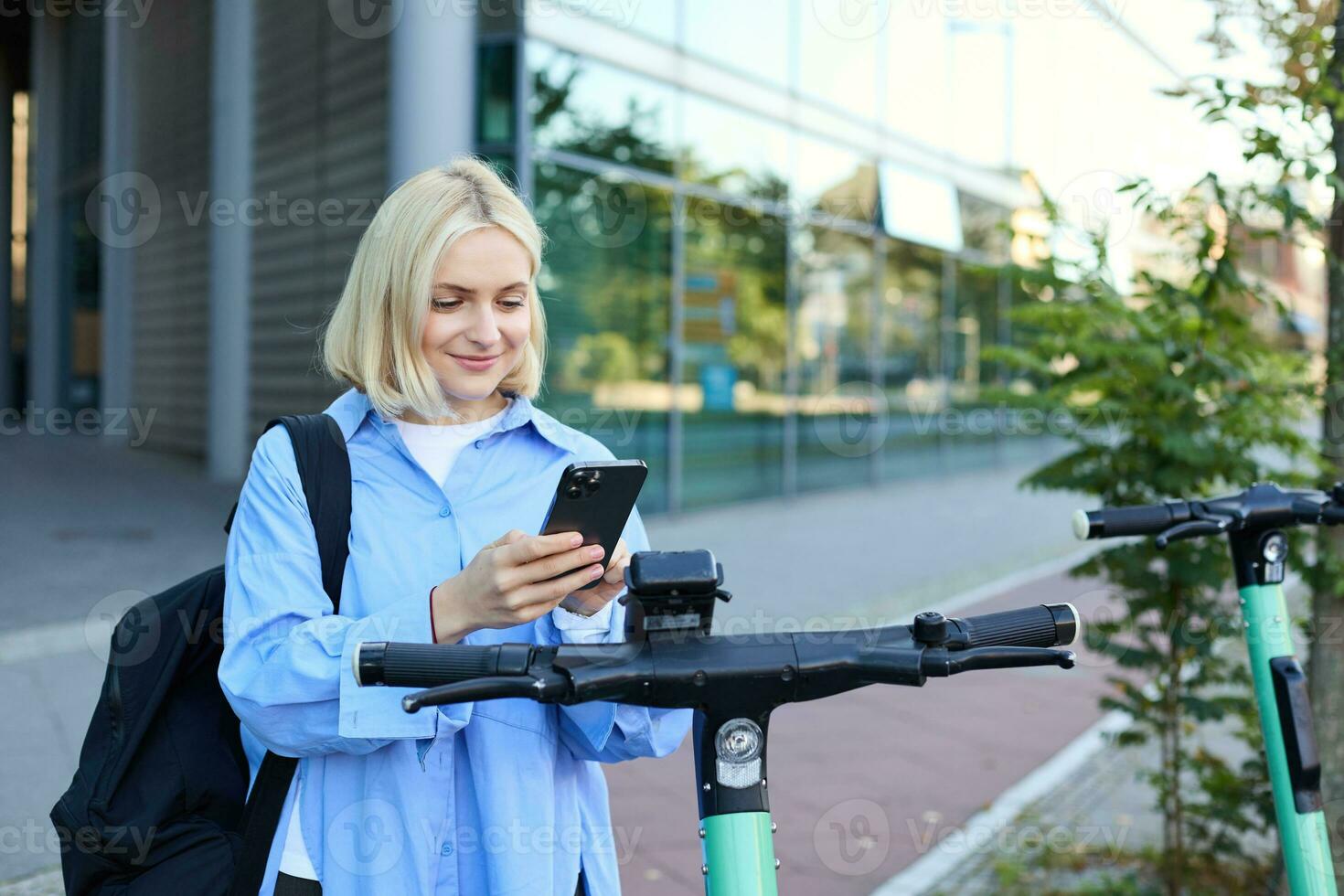 Portrait of young woman, renting a scooter, using mobile phone app to unlock it, using quick ride to get to work, smiling and looking happy photo