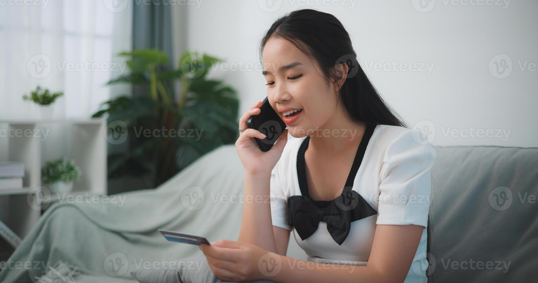 Portrait of Young asian woman sitting on sofa in living room, makes online banking payments through the internet from bank card on smartphone ,Shopping online with credit card. photo
