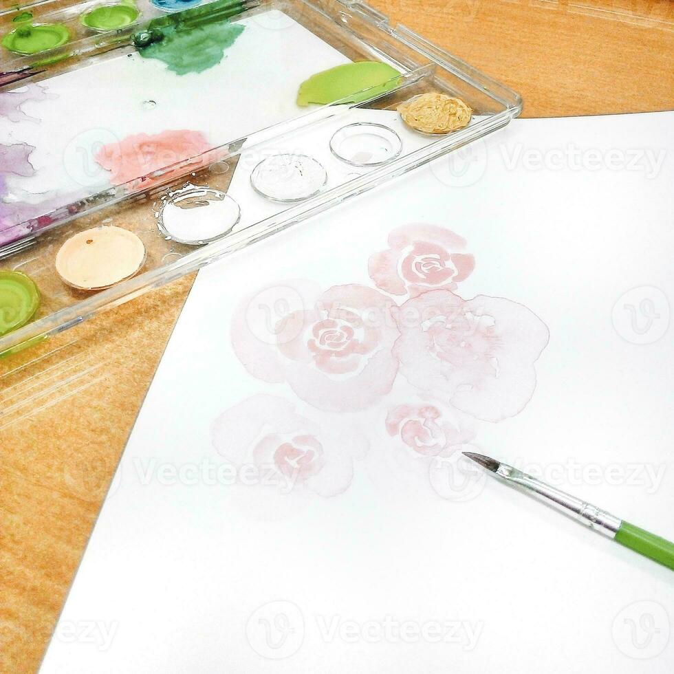 Watercolor paints and brushes on white paper with watercolor roses. photo