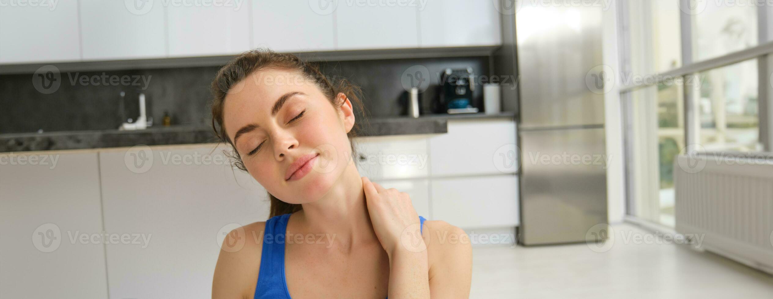 Close-up potrait of fitness woman, does training, workout from home, massaging neck, exercise in living room photo