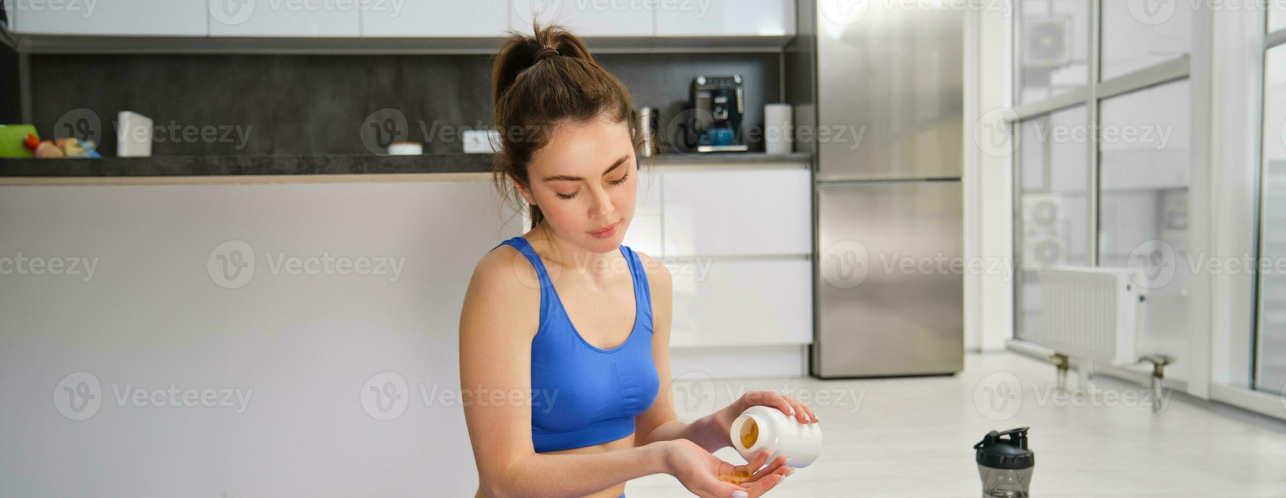 Portrait of beautiful and healthy fitness woman, taking vitamins, dietary supplements for muscles and bones, doing workout training at home photo