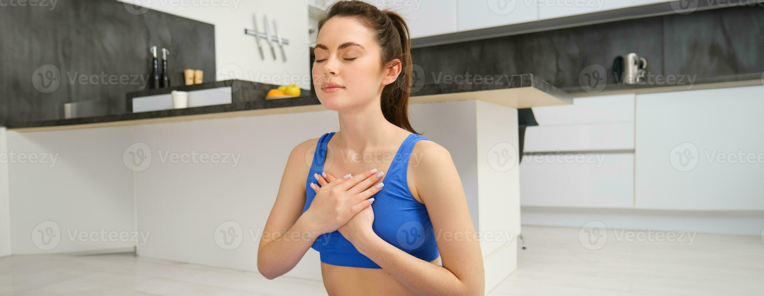 Woman practicing yoga and meditation at home sitting in lotus pose on yoga mat, relaxed with closed eyes. Mindful meditation concept. Wellbeing photo