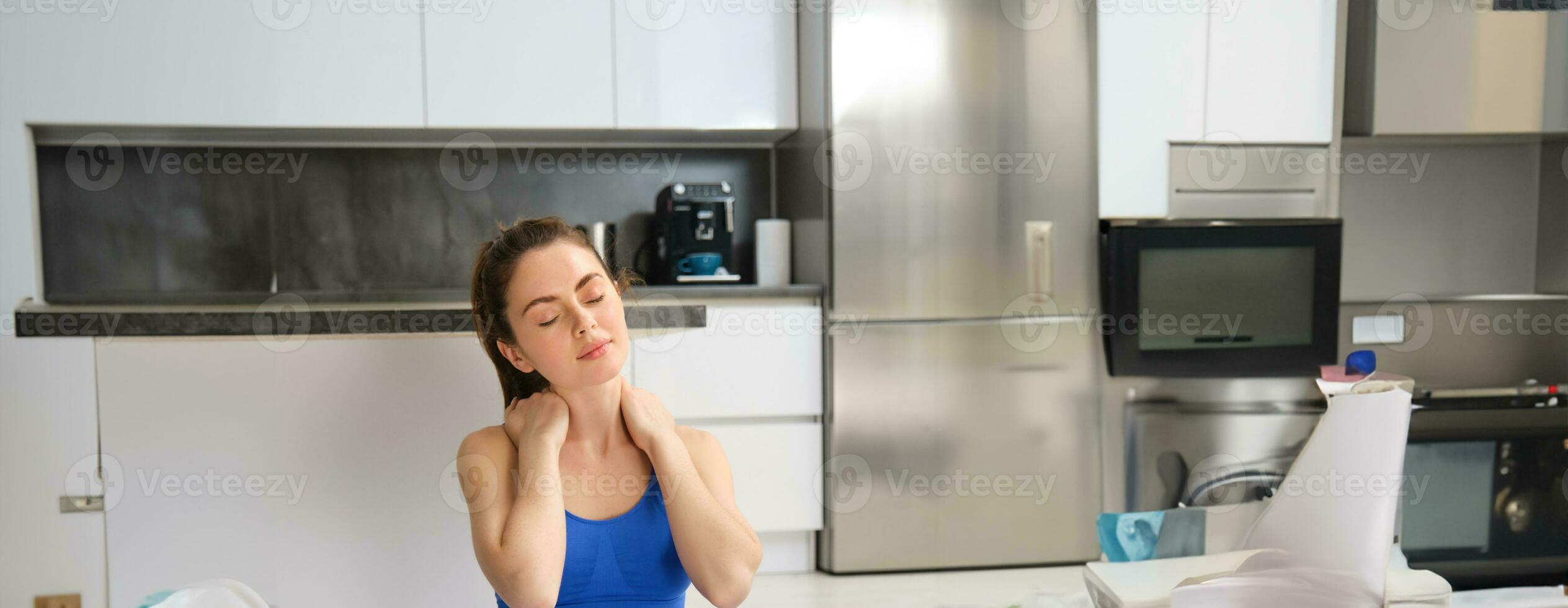 Portrait of woman workout from home, does training exercises, stretches her neck, warm-up before fitness photo