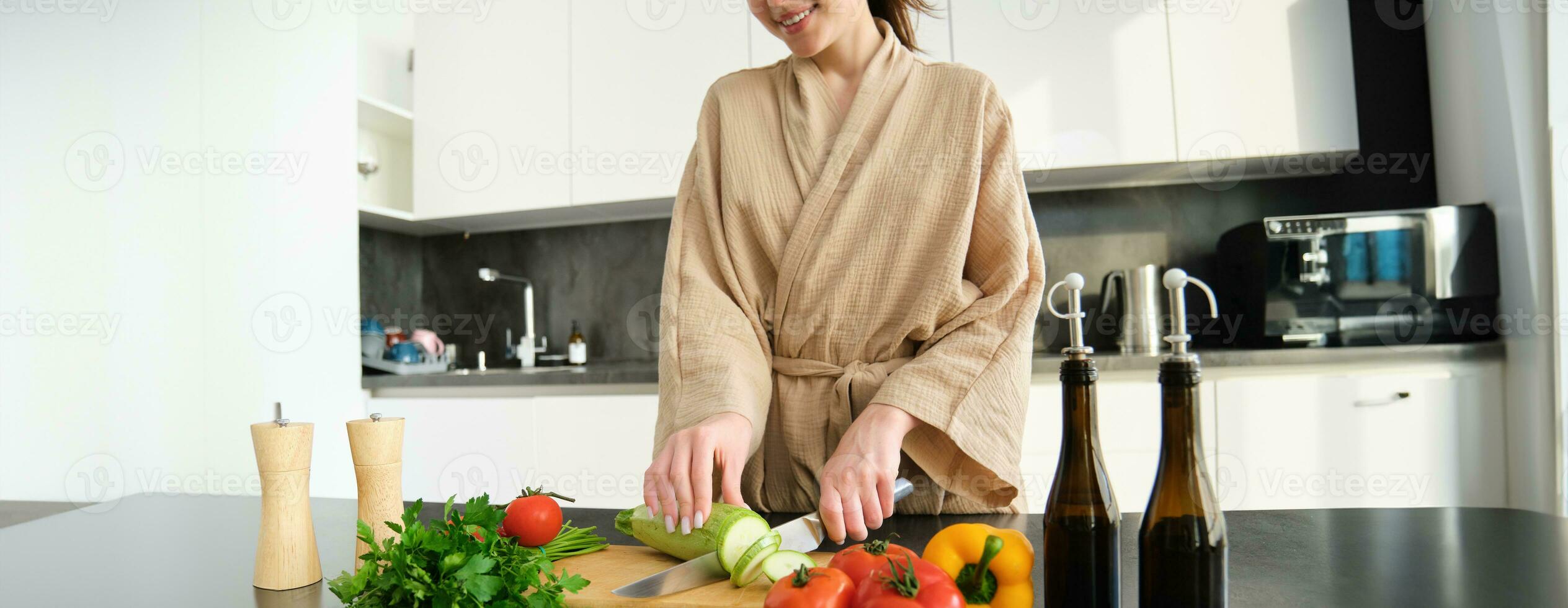 Healthy lifestyle. Young woman in bathrobe preparing food, chopping vegetables, cooking dinner on kitchen counter, standing over white background photo